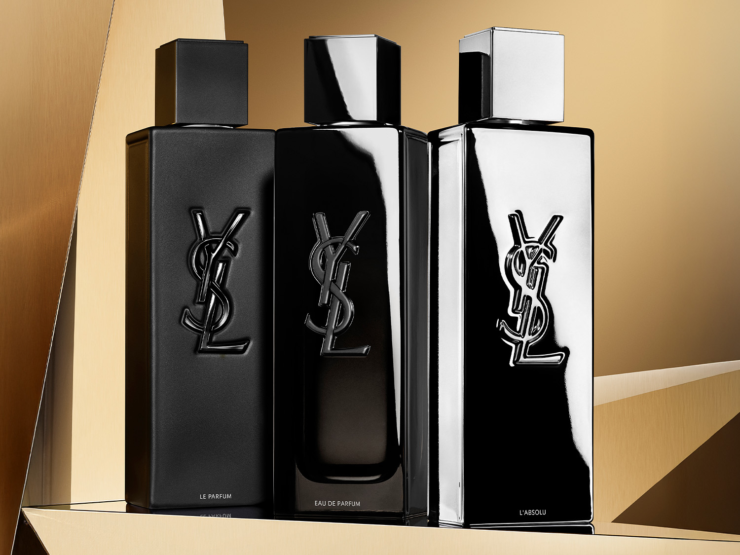 Trzy flakony perfum YSL w czarnych, błyszczących butelkach z logo marki, prezentujące różne warianty zapachowe: Le Parfum, Eau de Parfum i L'Absolu.