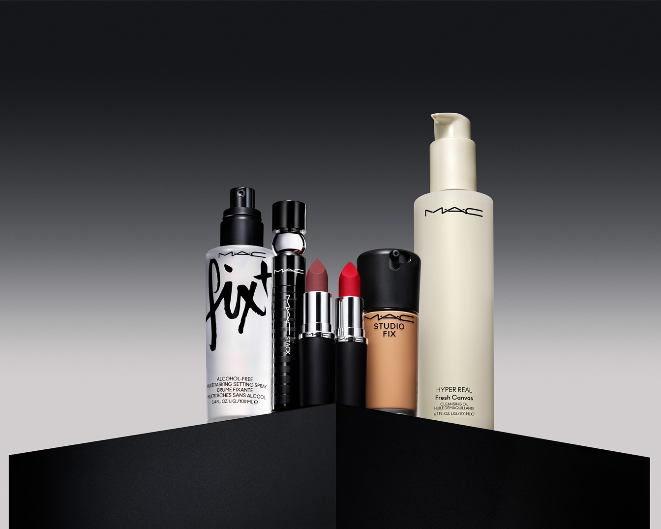 Sechs MAC-Produkte, darunter Fix+, die Studio Fix Fluid Foundation und das Hyper Real Fresh Canvas Cleansing Oil, werden auf einem eleganten, abgestuften Display präsentiert.