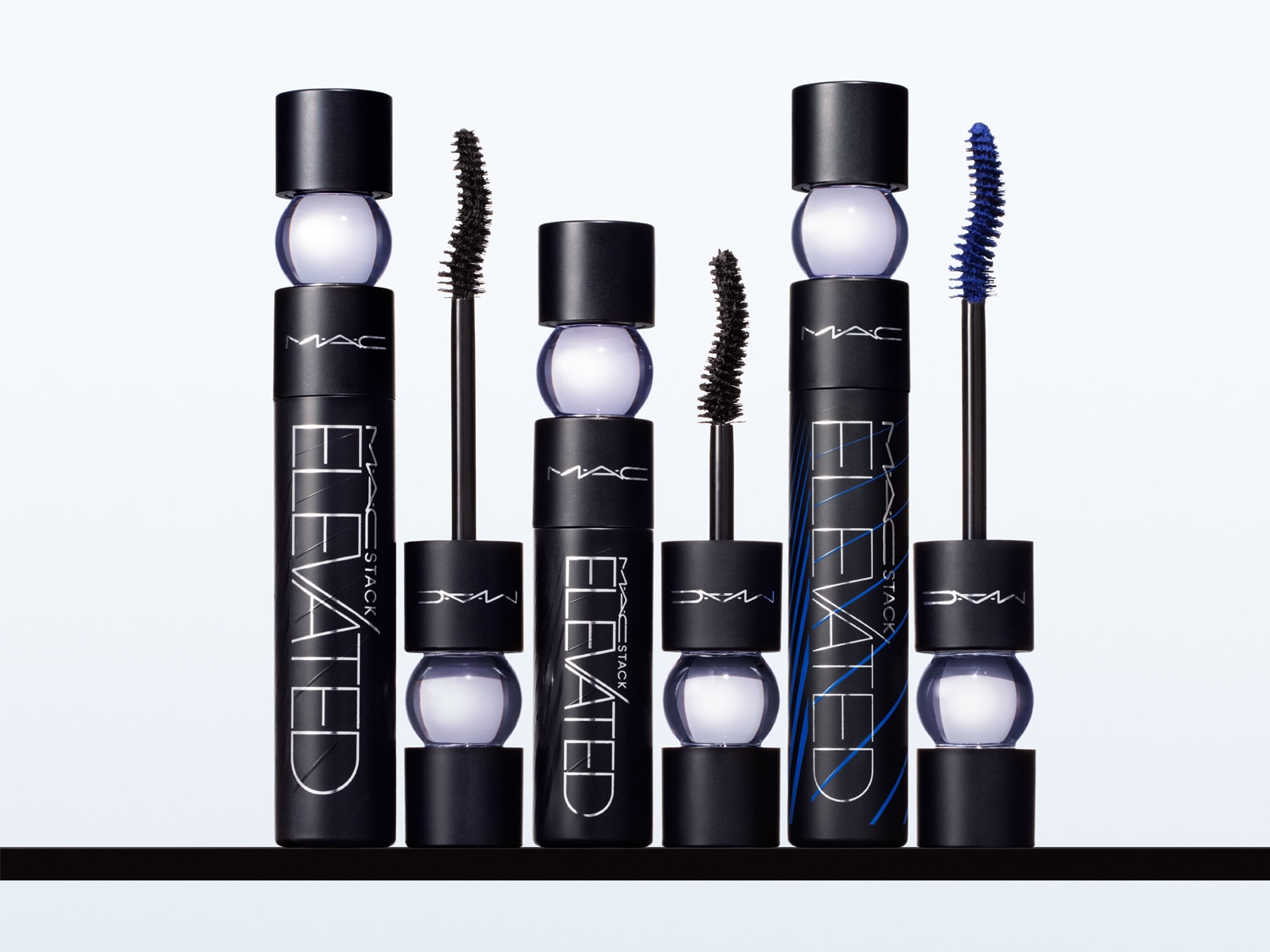 Mehrere geschlossene und geöffnete Tuben der MAC Elevated Stack Mascara in verschiedenen Farbtönen, schwarz und blau, stehen nebeneinander aufgereiht.