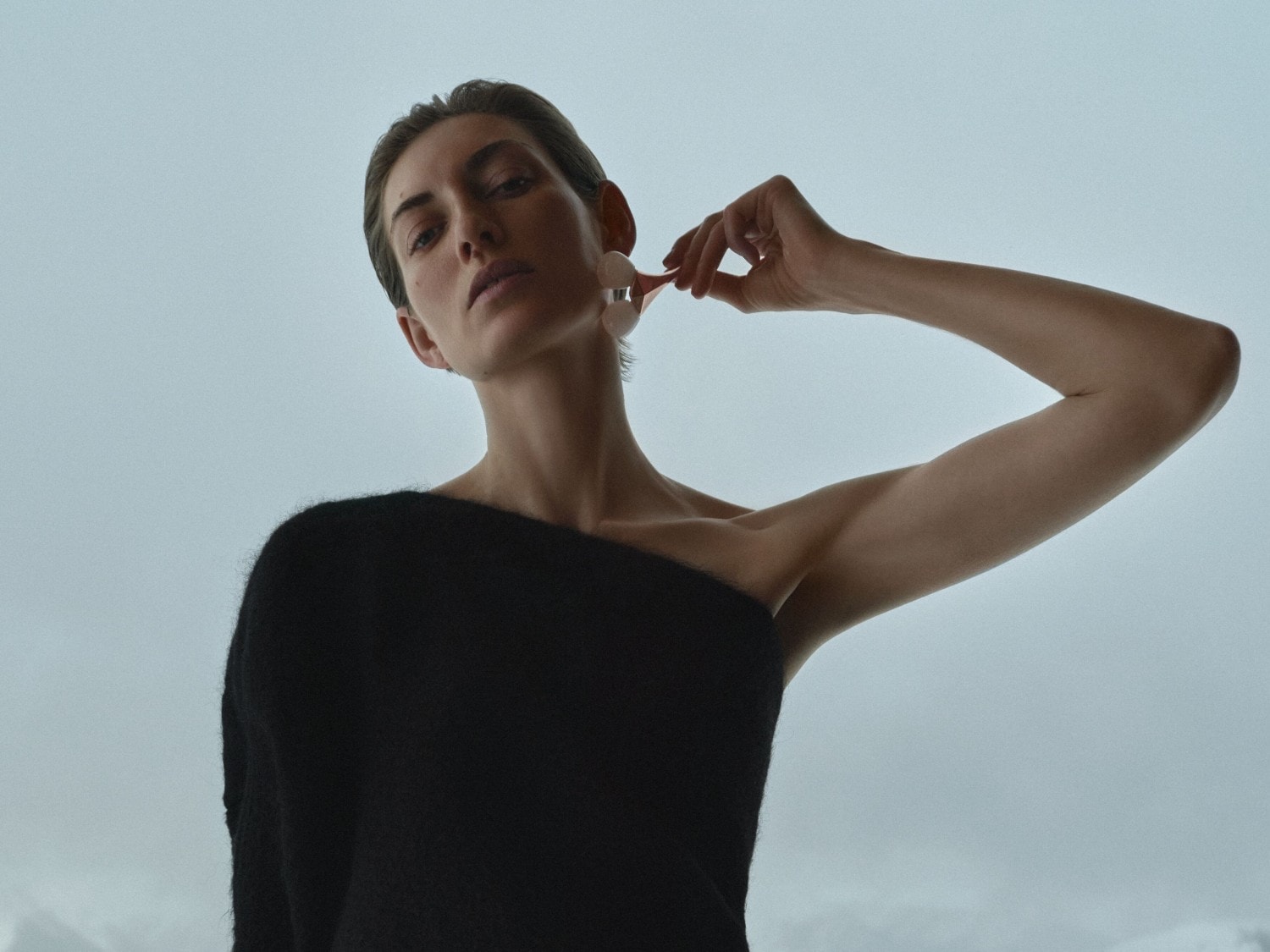 Eine Frau mit einem schwarzen Oberteil und Ohrringen, die ein rundes, hellrosa Accessoire an ihrem Ohr hält.