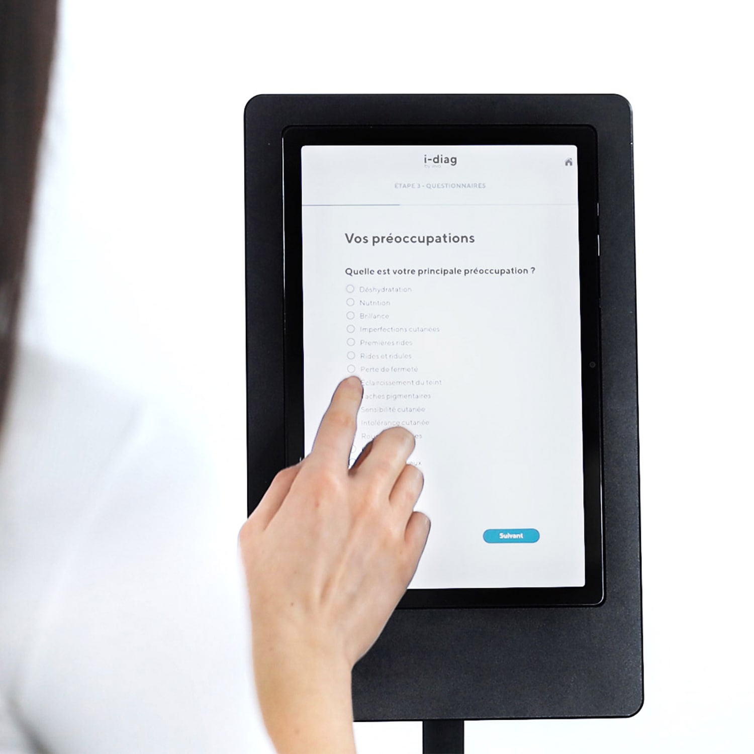 Un touch screen nero mostra un questionario di bellezza dove una mano seleziona una risposta, aiutando a personalizzare la tua routine di bellezza.