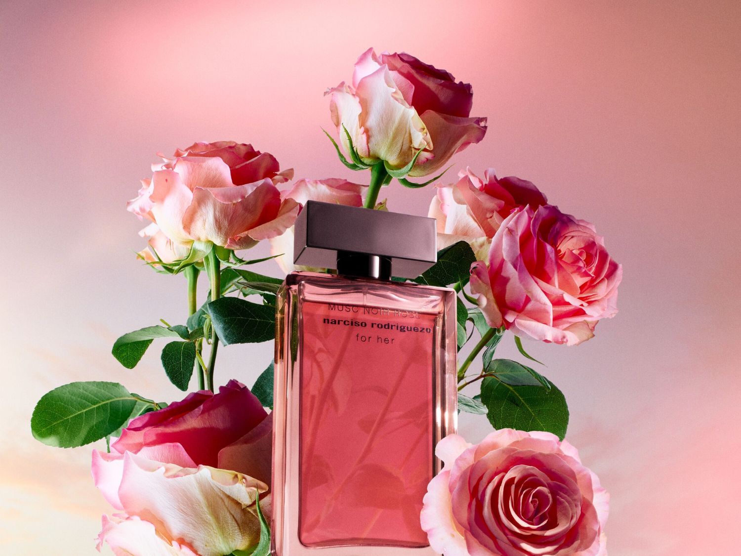 Roze Narciso Rodriguez for Her parfumfles omringd door rozen, een elegante combinatie van bloemige en muskusachtige noten.