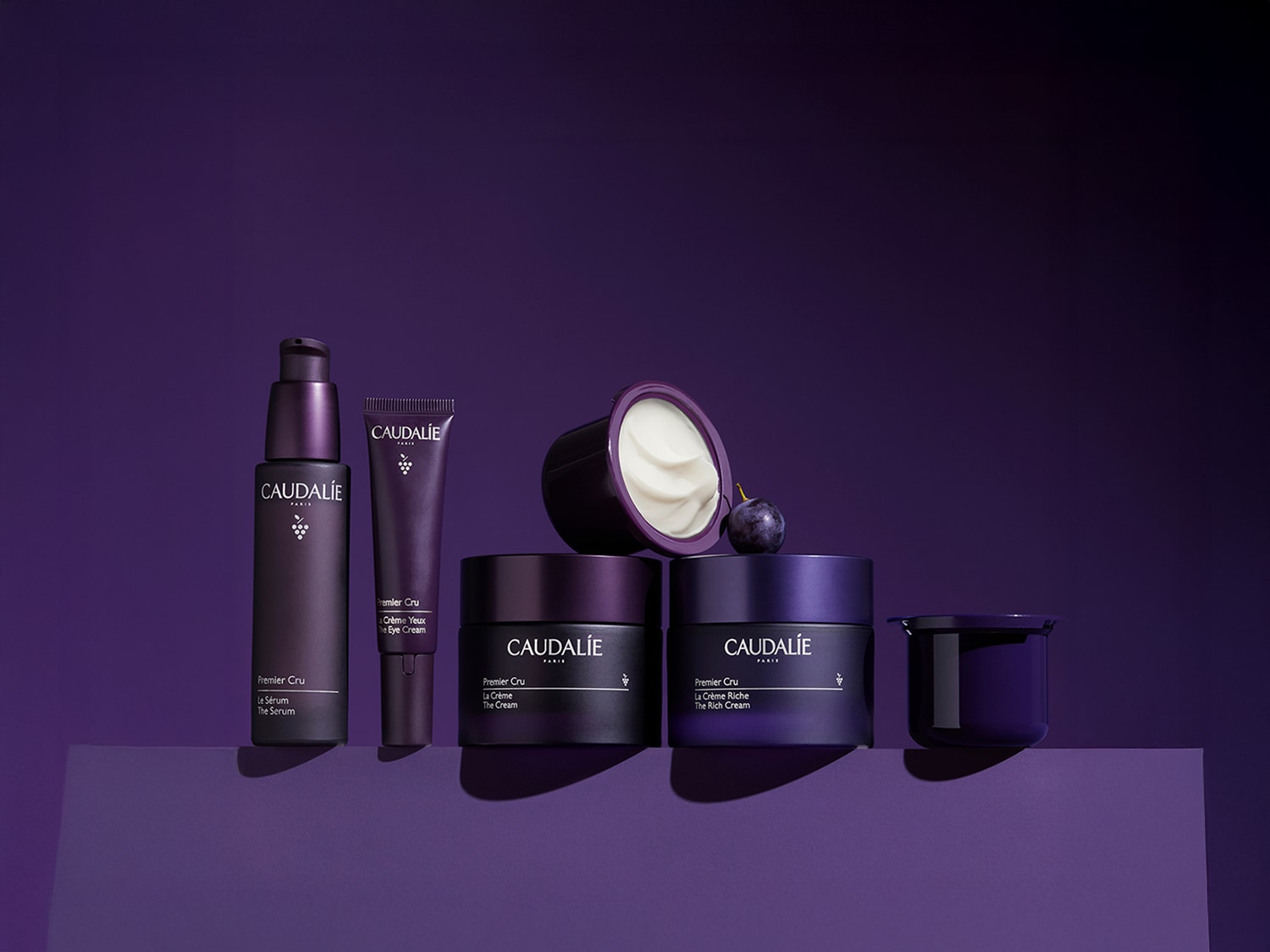 Eine Auswahl an Premier Cru Hautpflegeprodukten von Caudalie in lila Verpackung, darunter Serum, Augencreme und Cremes, die auf einer abgestuften lila Oberfläche präsentiert werden.