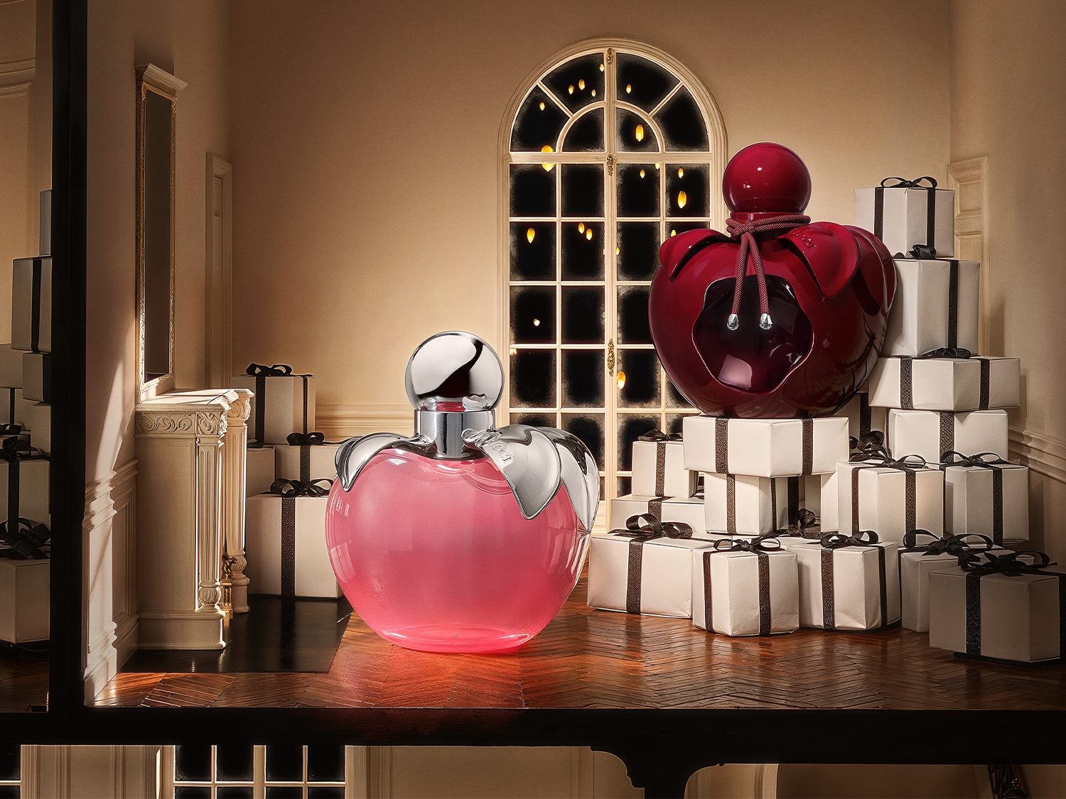 Découvrez les parfums Nina et Nina Rouge de Nina Ricci, présentés dans des flacons en forme de pomme rose et rouge, entourés de cadeaux blancs élégants.