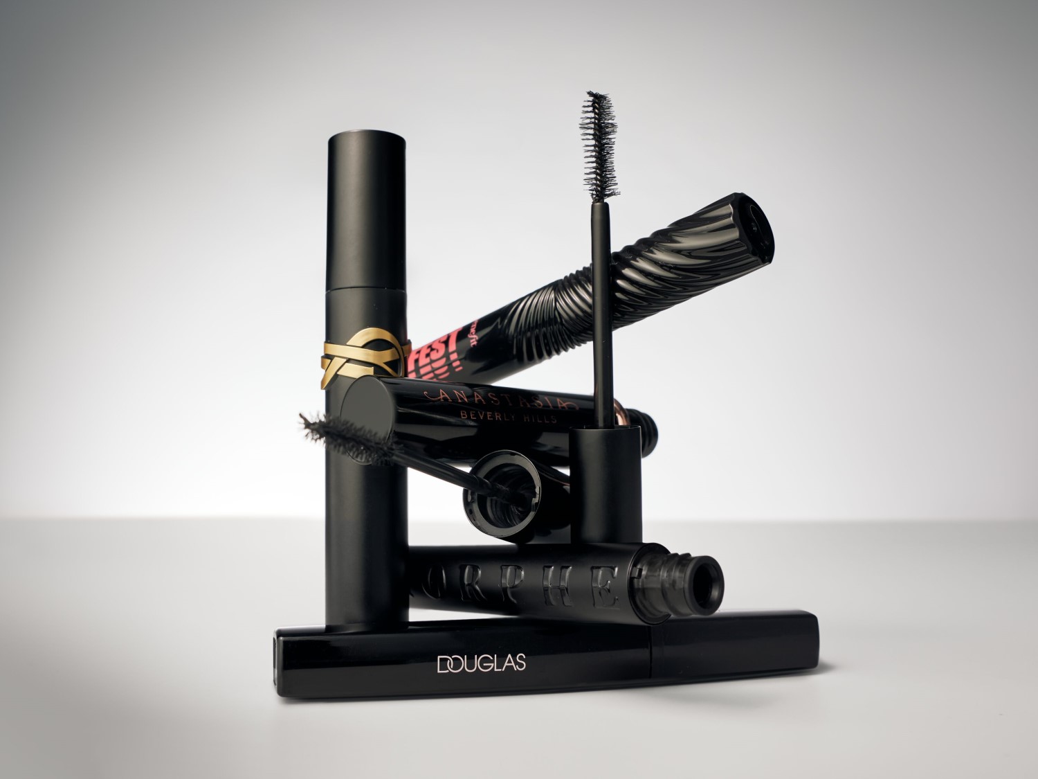 Een stapel zwarte mascara's van verschillende merken, waaronder Yves Saint Laurent, Anastasia Beverly Hills, Orphée en Douglas.