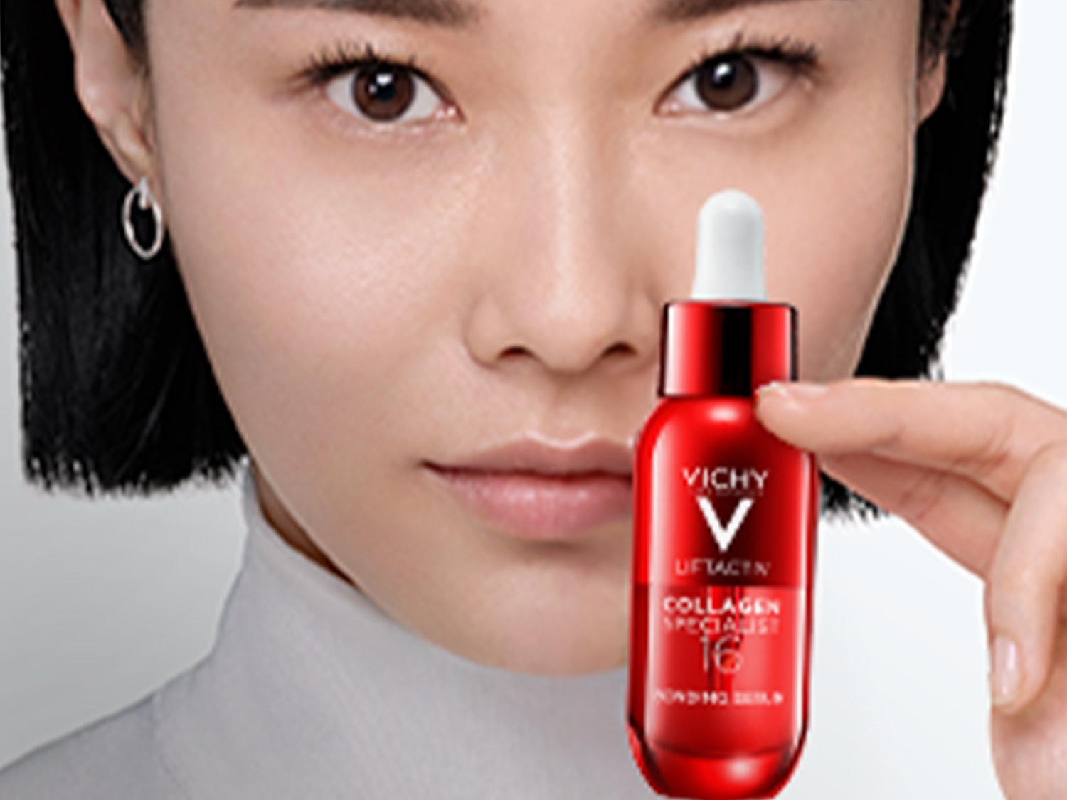 Primo piano di una donna che tiene in mano un flacone rosso di siero Vichy Liftactiv Collagen Specialist con contagocce bianco, promuovendo la cura della pelle.