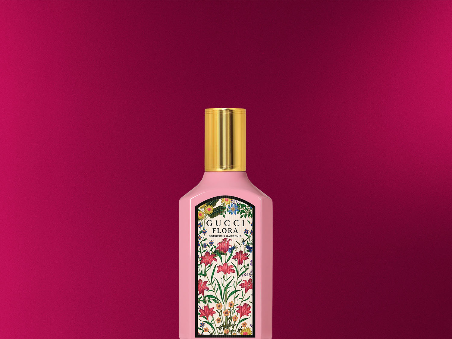 Ružový flakón parfému Gucci Flora Gorgeous Gardenia s kvetinovým vzorom a zlatým vrchnákom na ružovom pozadí.