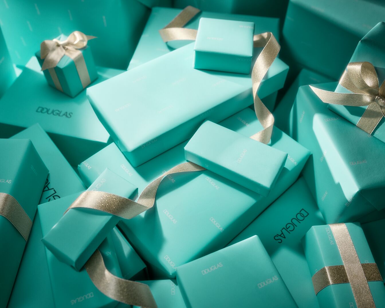 Een stapel turquoise Douglas-geschenkdozen, sommige versierd met gouden linten, klaar om uit te pakken en te genieten.