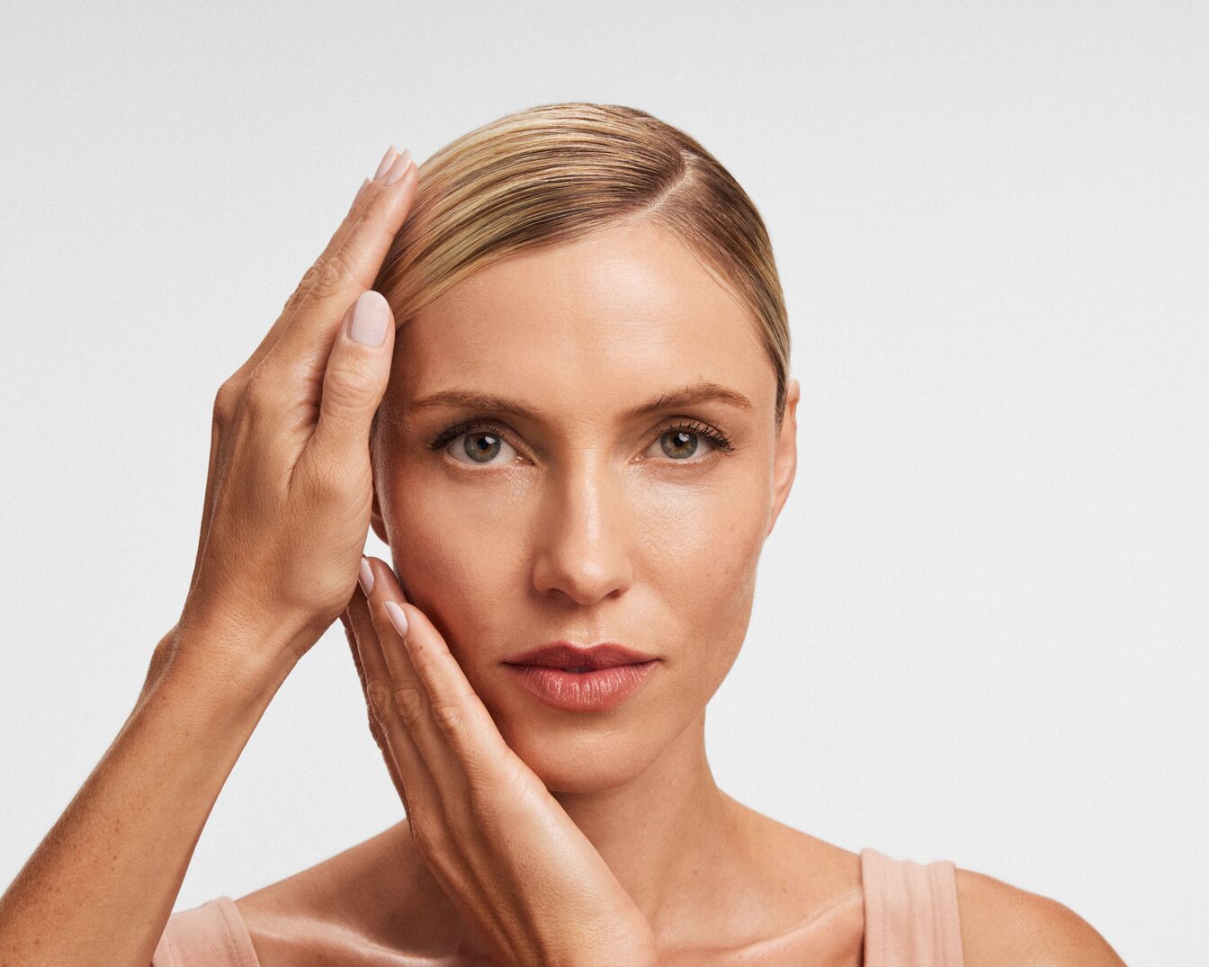 Nahaufnahme einer Frau mit blonden Haaren, die ihre Hände auf ihr Gesicht legt und eine sanfte, gepflegte Haut zeigt.