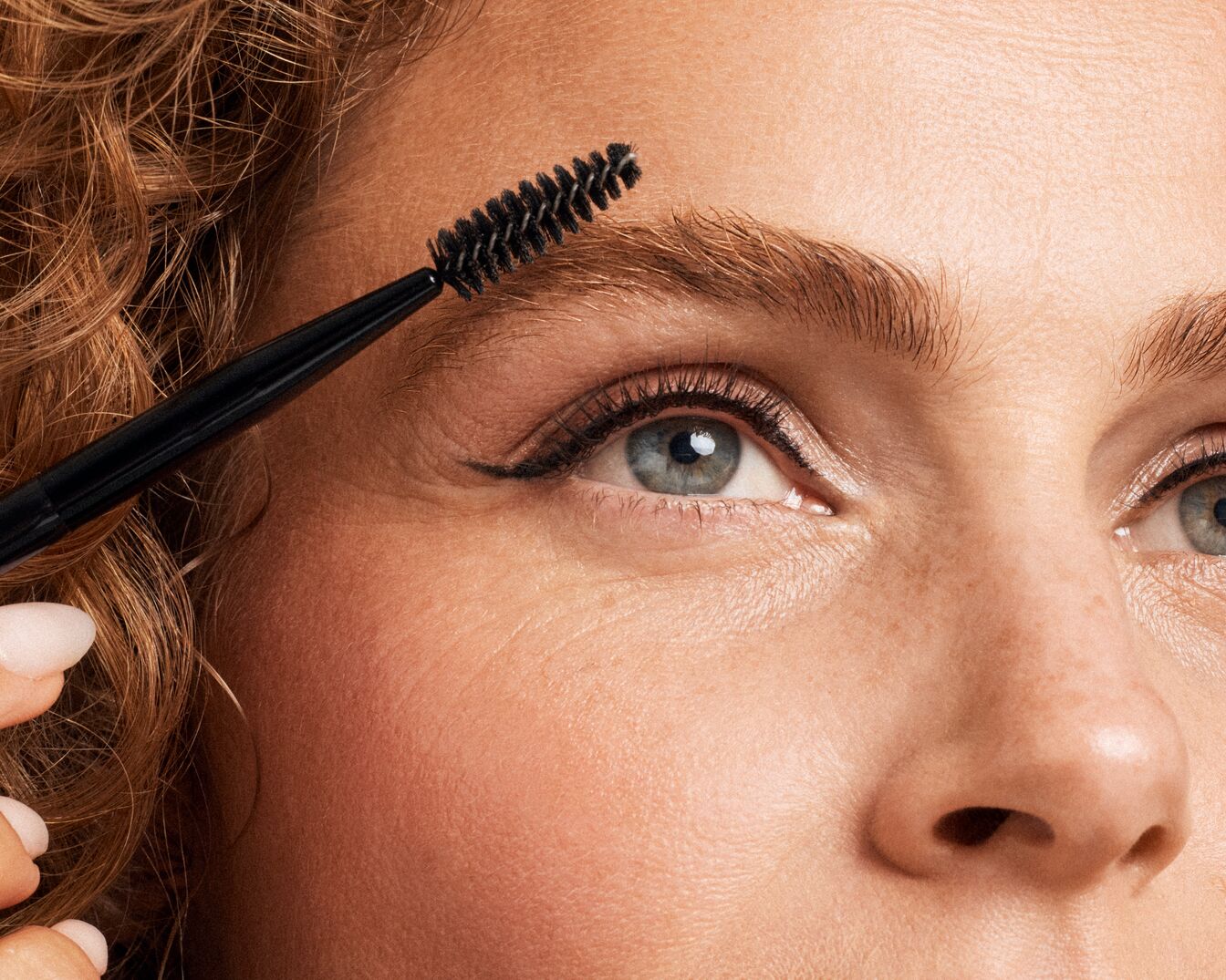 Nahaufnahme einer Frau, die ihre Augenbrauen mit einer schwarzen Bürste kämmt, um einen gepflegten Look zu erzielen.