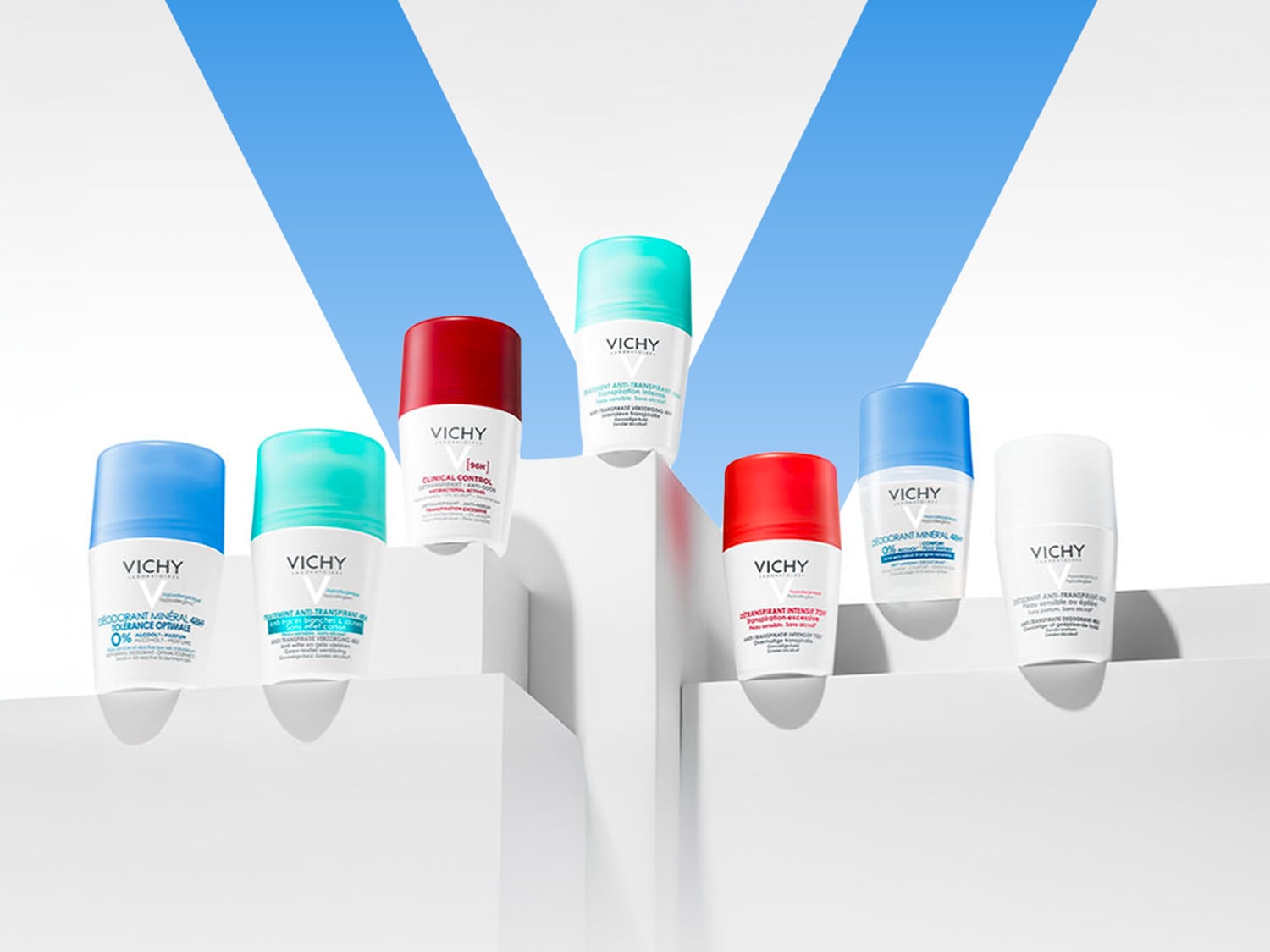 Une collection de déodorants roll-on Vichy aux bouchons colorés bleu, turquoise, rouge et blanc, présentés sur des socles blancs avec un fond bleu et blanc.