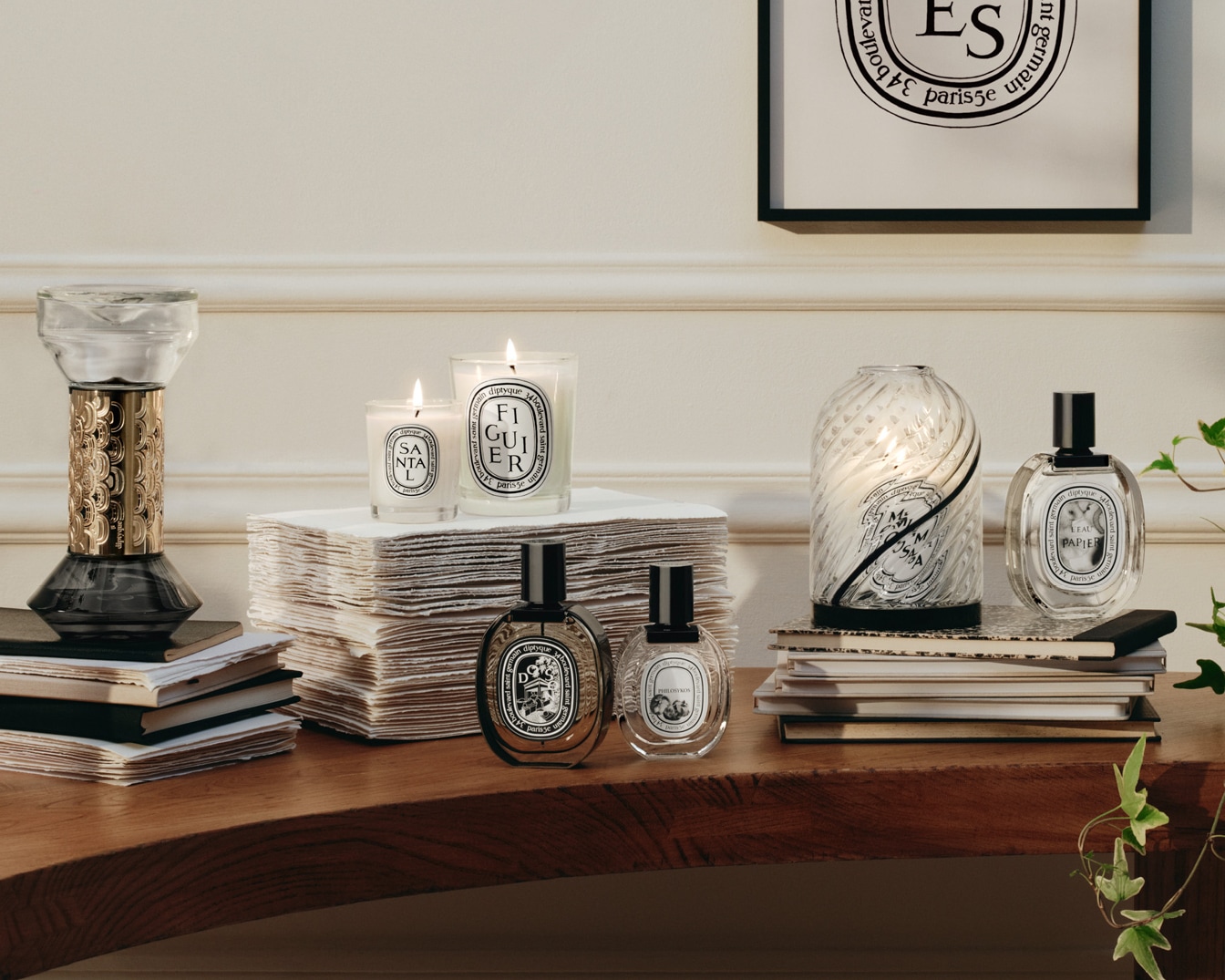 Eine Sammlung von Diptyque-Duftkerzen und verschiedenen Parfums, die auf einem Holztisch mit Büchern und dekorativen Elementen arrangiert sind.