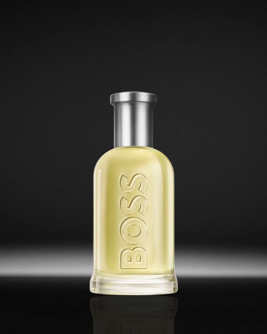 Gele BOSS parfumfles met zilveren dop, de naam 'BOSS' staat verticaal op de fles.