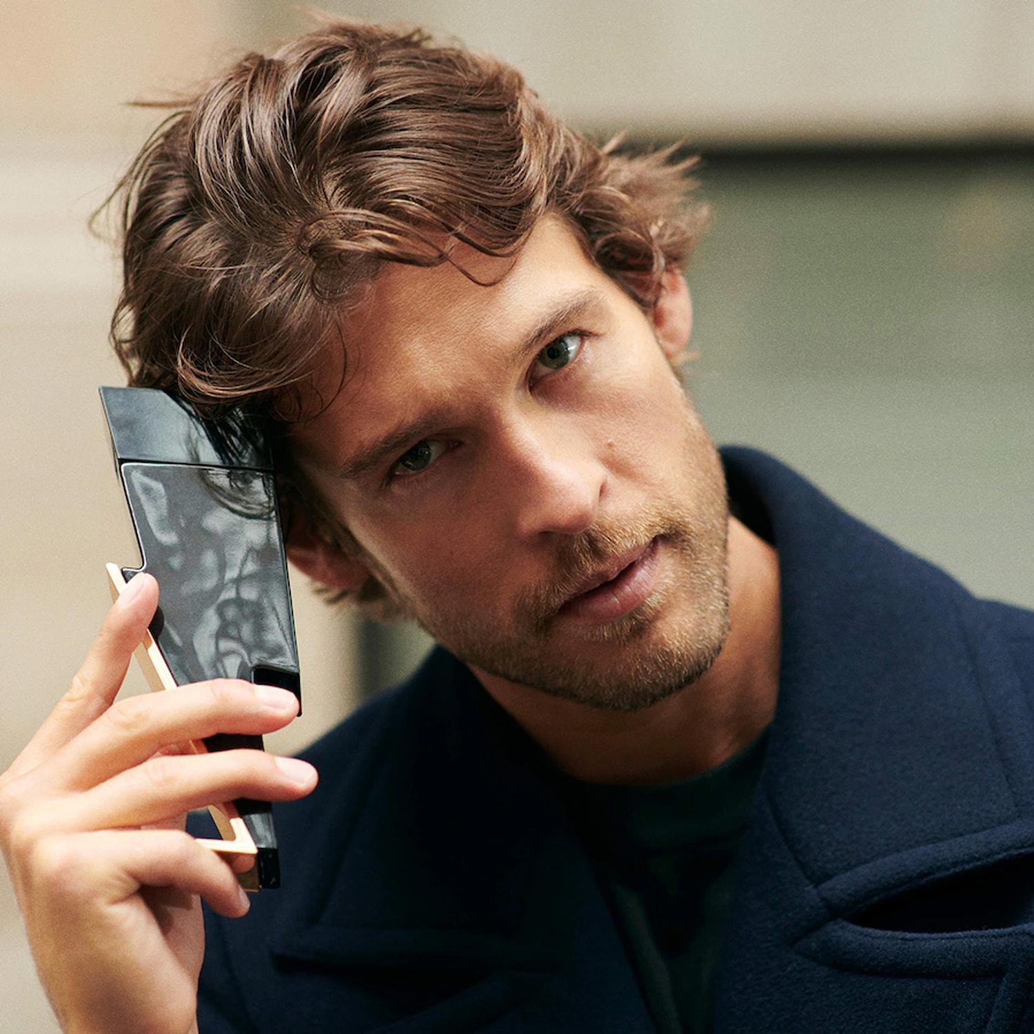 Mężczyzna z brązowymi włosami trzyma flakon perfum w kształcie czarnego pioruna z elementami złota, prezentując zapach.