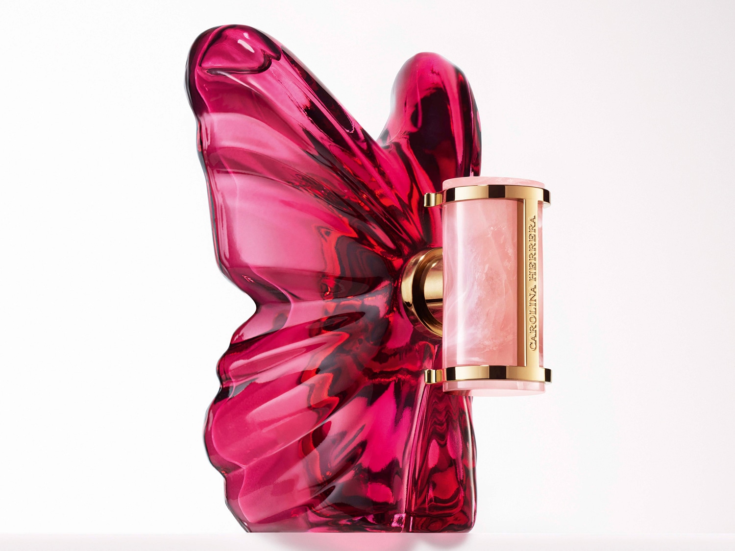 Butelka perfum Carolina Herrera w kształcie różowego motyla z cylindrycznym flakonem o złotych akcentach, emanująca luksusem i kobiecością.