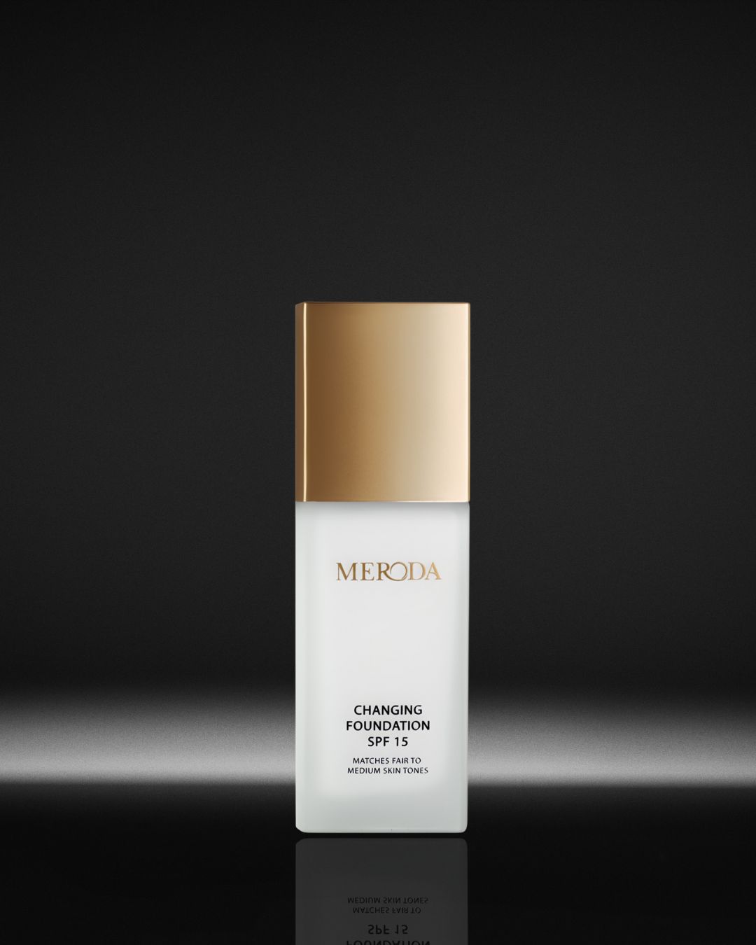 Le fond de teint changeant SPF 15 de Meroda s'adapte aux teints clairs à moyens, présenté dans un flacon blanc avec un bouchon doré.