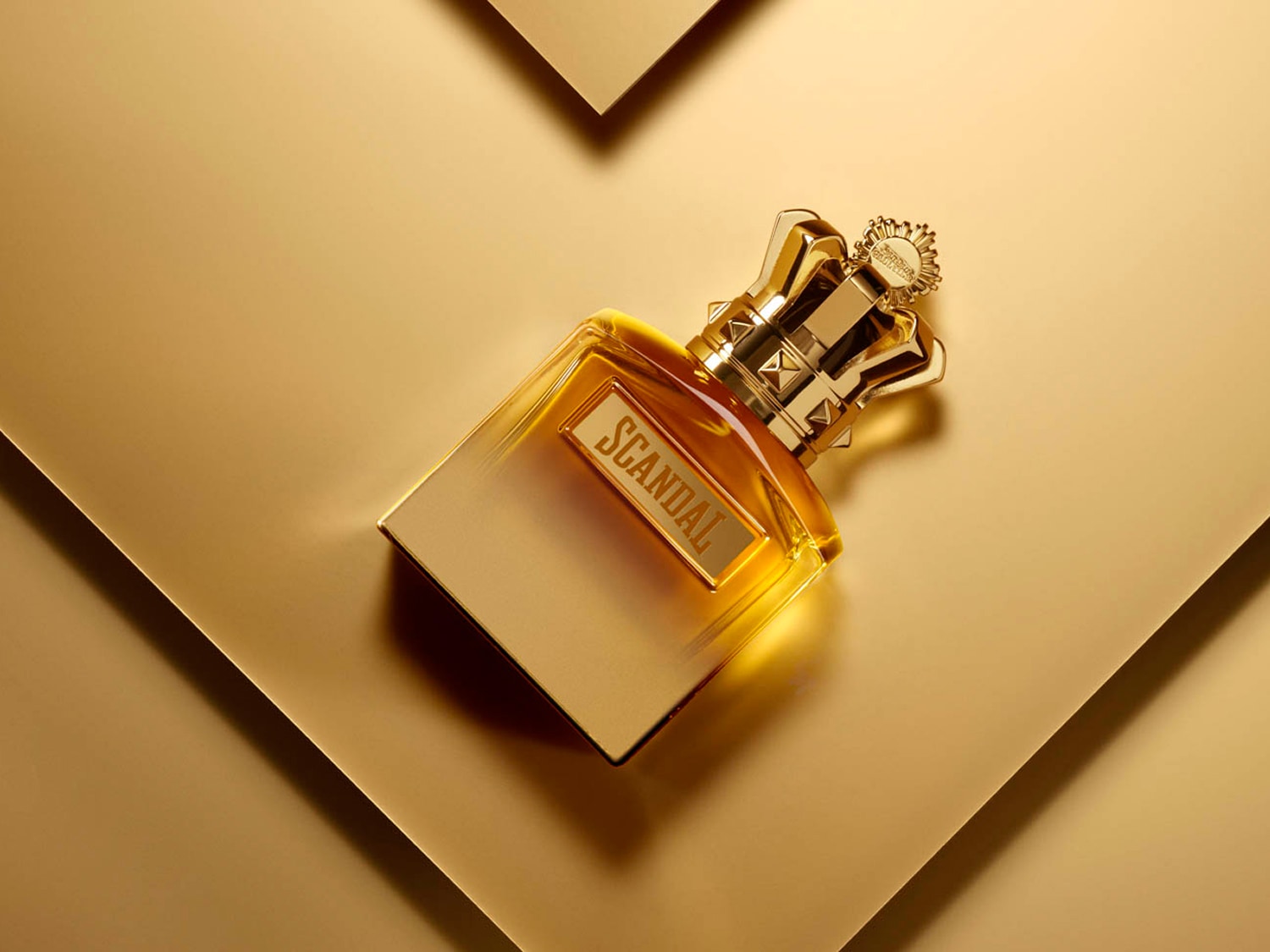 Złoty flakon perfum Scandal z koroną na złotym tle emanuje luksusem i wyrafinowaniem.
