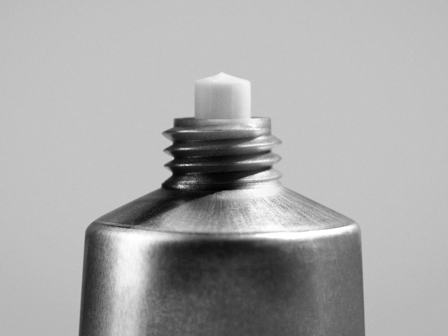 Grijstint close-up van een metalen tube met een witte, zeshoekige opening, klaar voor gebruik.