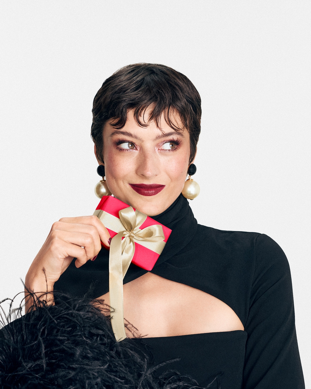 Une femme élégante en noir tient un cadeau rose avec un ruban doré, parfaite pour offrir un moment de beauté.