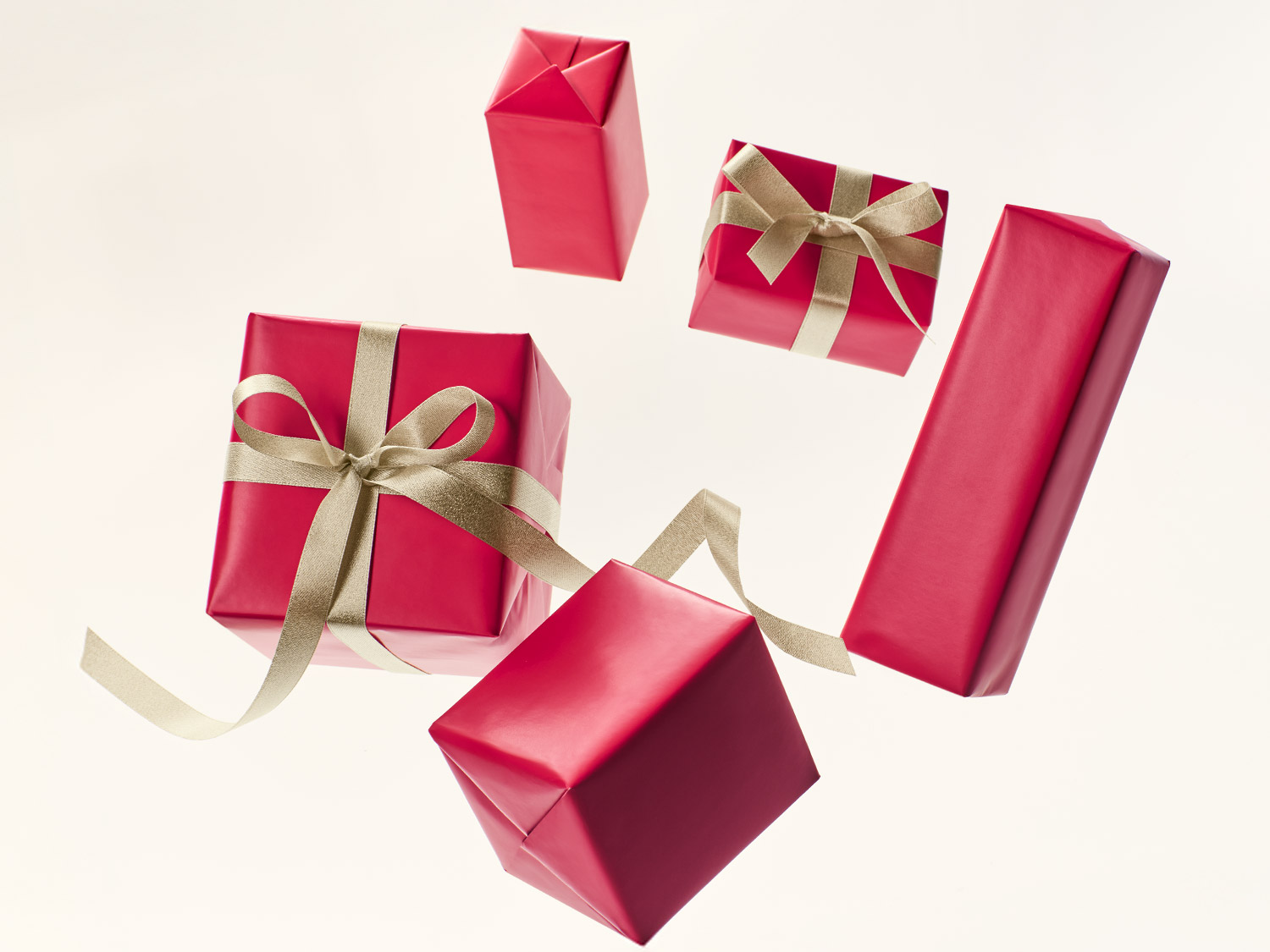 Divers cadeaux emballés dans du papier rouge vif et ornés d'élégants rubans dorés, flottant sur un fond clair et uni.