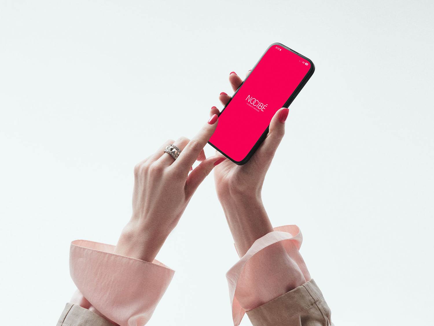 Maintenant, magasinez vos produits de beauté préférés sur l'application Nocibé, présentée sur un téléphone à écran rose vif tenu par une main manucurée.