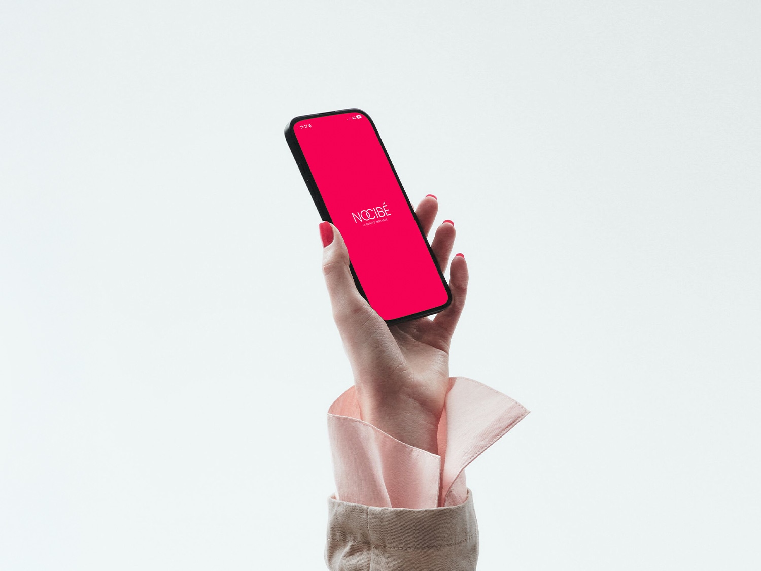 Main tenant un smartphone avec l'écran rose vif affichant le logo Nocibé, sur un fond blanc épuré.