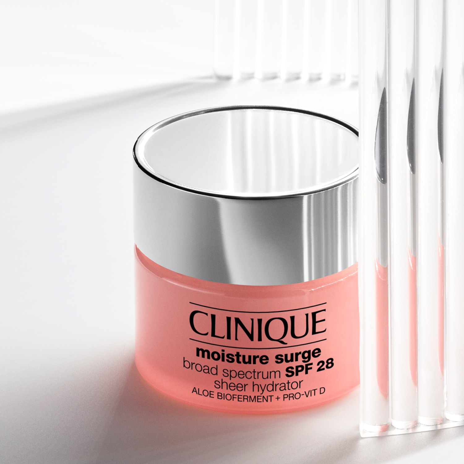 Voici un pot de crème hydratante Clinique Moisture Surge avec un couvercle argenté, offrant une protection solaire SPF 28 et enrichie en aloe biofermenté et pro-vitamine D.