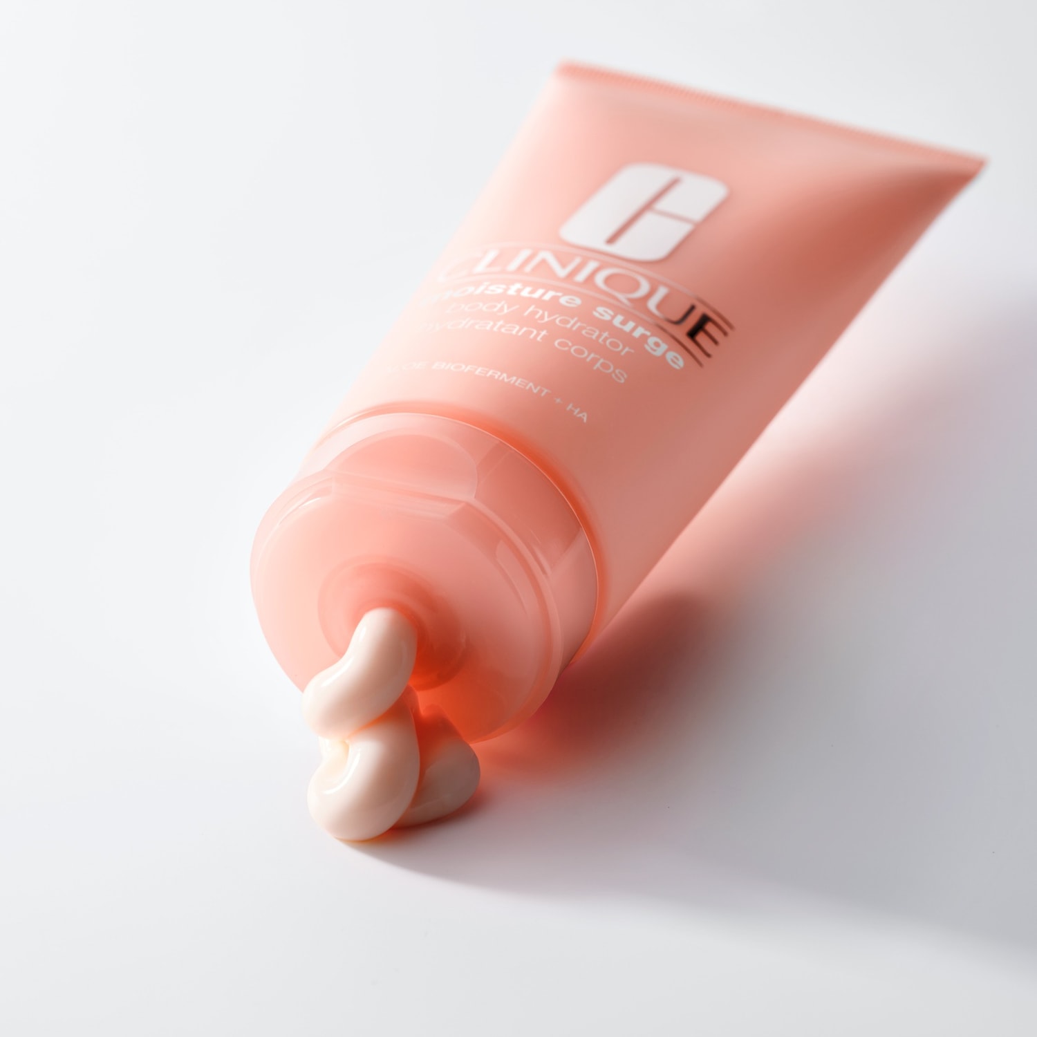 Voici un tube rose pêche de Clinique Moisture Surge Body Hydrator, avec une crème hydratante qui sort du tube.