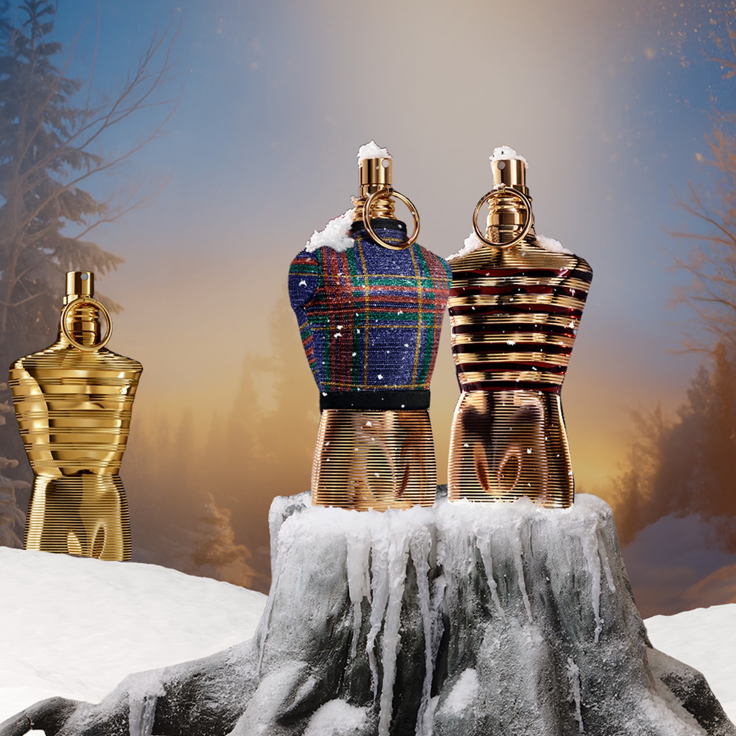 Dans un paysage hivernal enneigé, trois flacons de parfum dorés se dressent, dont deux vêtus de motifs festifs, évoquant l'esprit des fêtes.