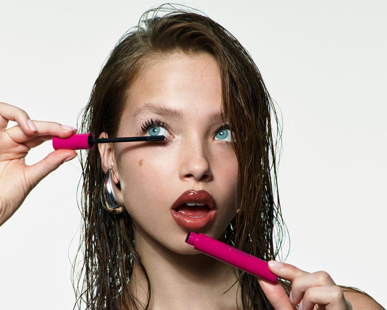 Primo piano di una modella con occhi azzurri che applica il mascara rosa sulle ciglia superiori per uno sguardo intenso.