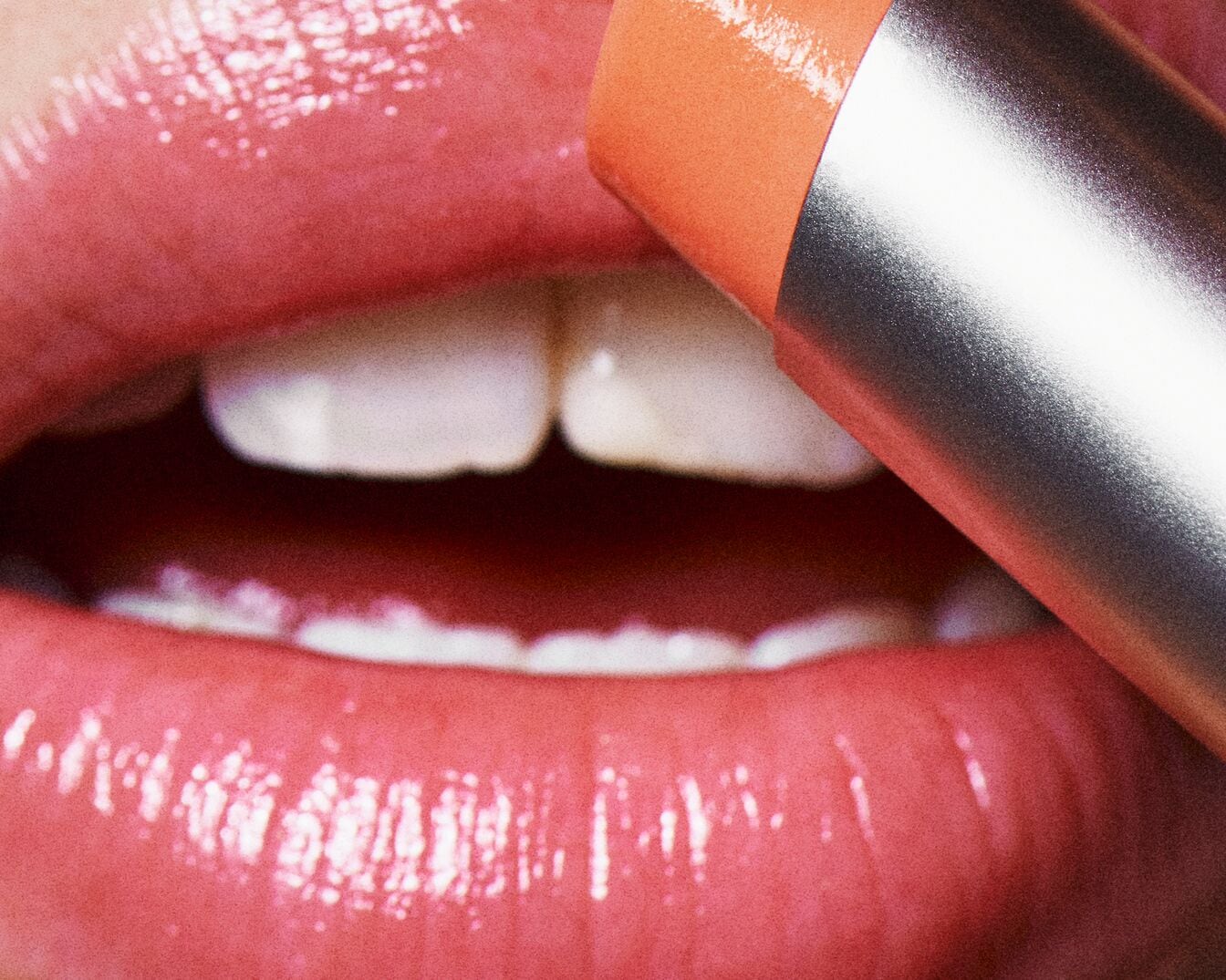 Primo piano di labbra lucide a cui viene applicato un rossetto color pesca dalla confezione argentata, per un look fresco e luminoso.