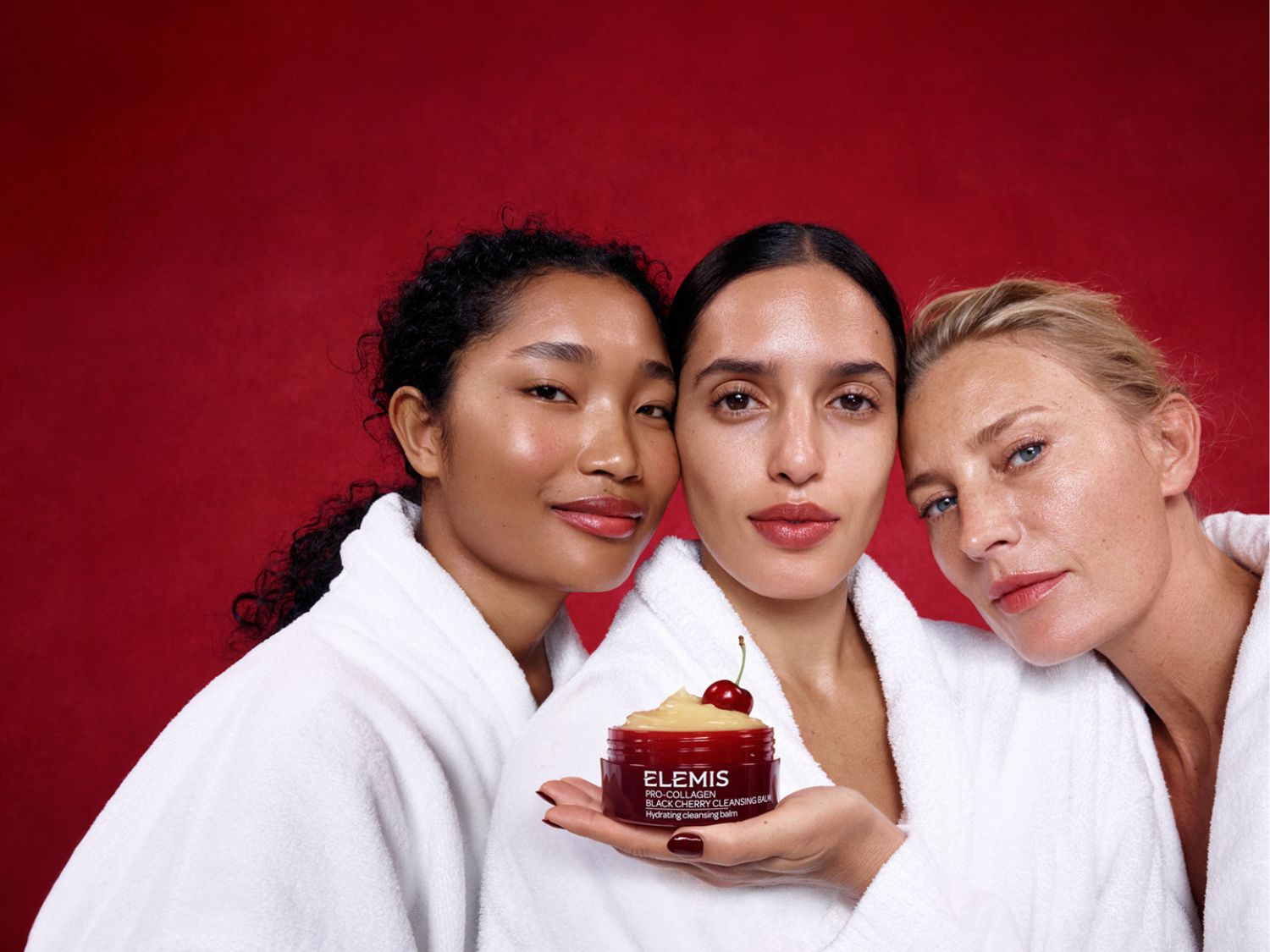 Tři ženy v bílých županech pózují s čisticím balzámem Elemis Pro-Collagen Black Cherry, který má na sobě třešeň.