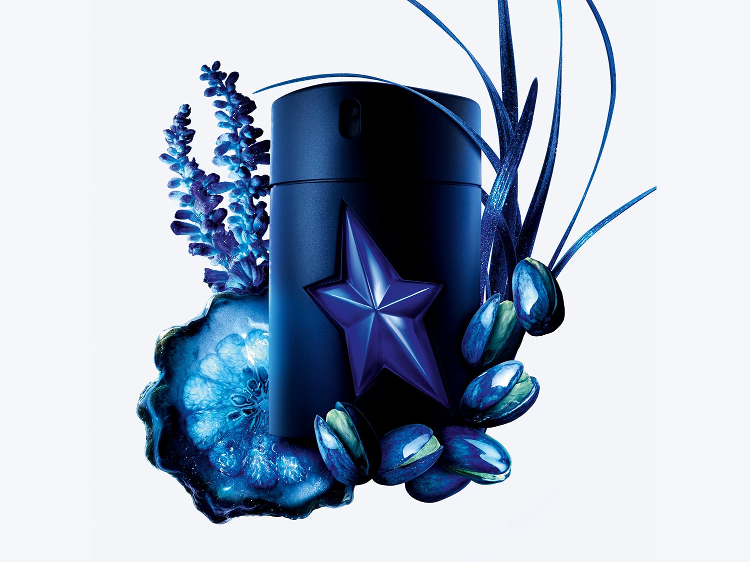Butelka ciemnoniebieskiego zapachu dla mężczyzn, ozdobiona gwiazdą, otoczona niebieskimi kwiatami, kamieniami i pistacjami na białym tle.