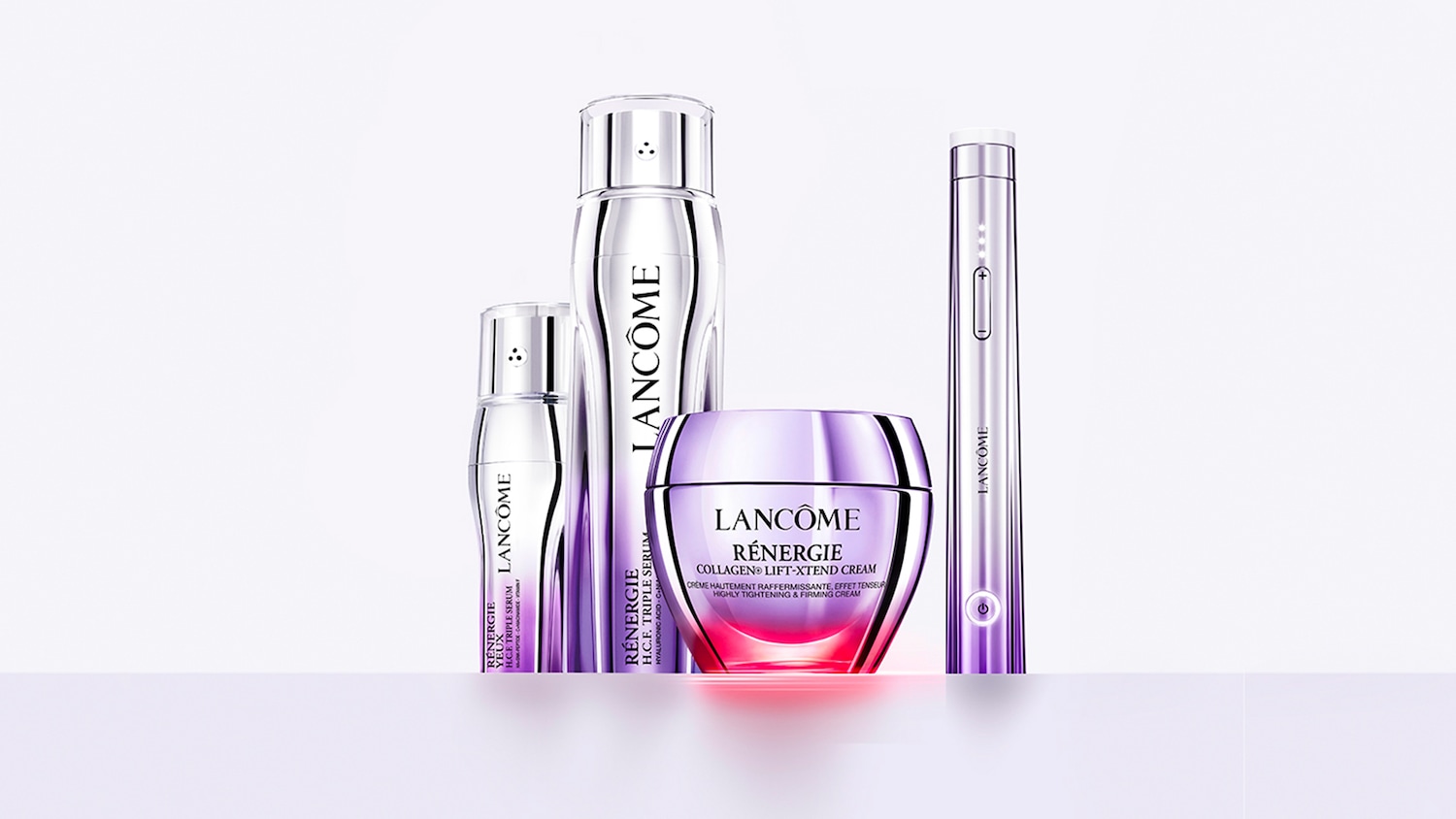 Close-up van vier Lancôme Rénergie huidverzorgingsproducten en een apparaat in zilver- en paarstinten, waaronder een crèmepot, serumflacons en een slank beautyapparaat, tegen een lichte minimalistische achtergrond.