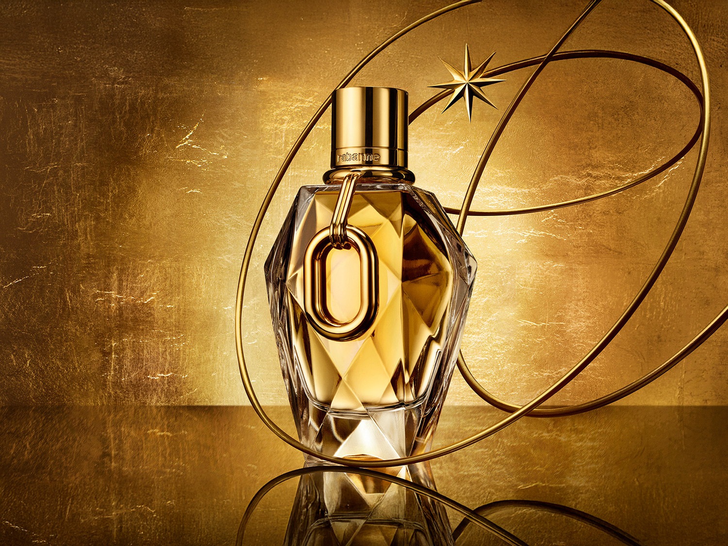 Gouden parfumfles van Rabanne, omringd door gouden lijnen en een ster, tegen een glanzende gouden achtergrond.