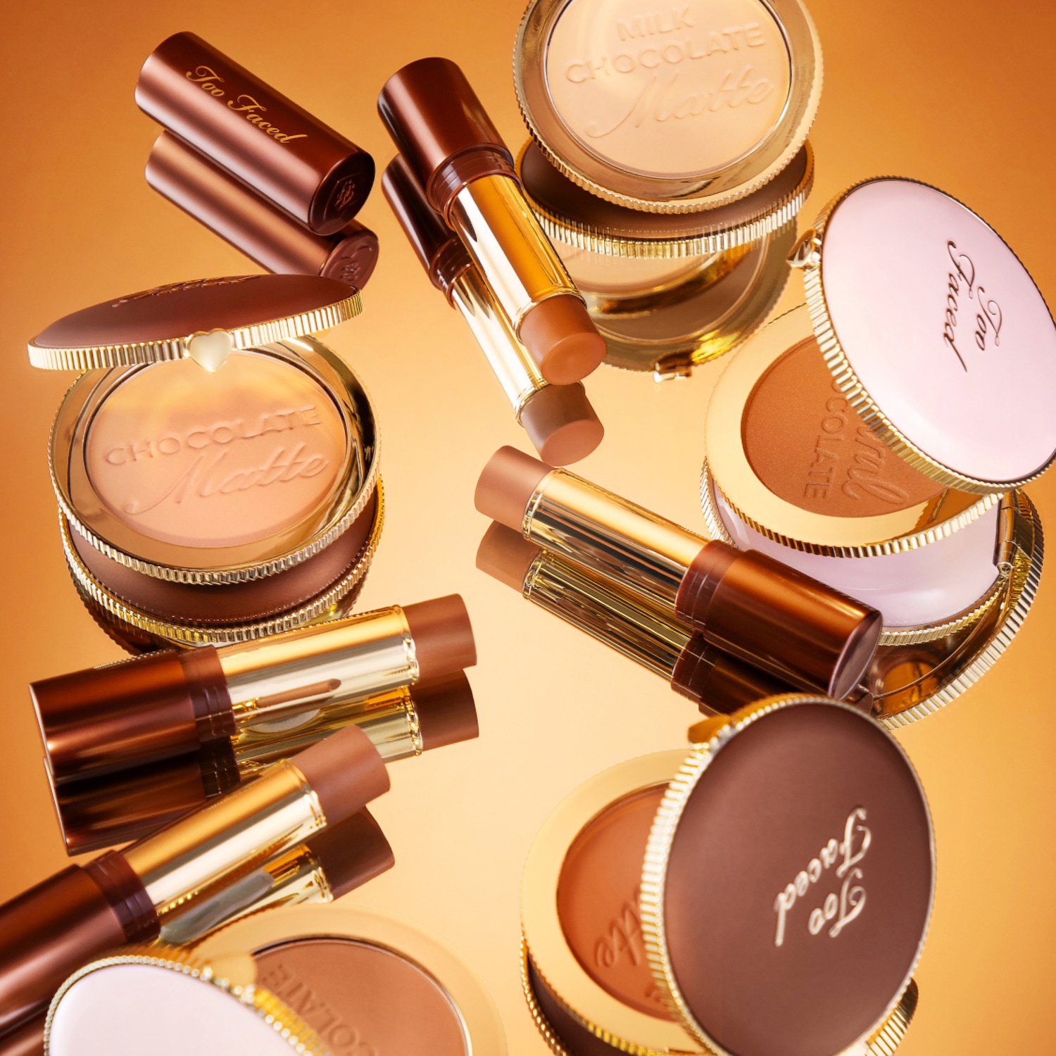 Mehrere Natural Chocolate Soleil Bronzer und Chocolate Soleil Melting Bronzing & Scultping Sticks liegen auf einem glänzenden, reflektierenden Untergrund.