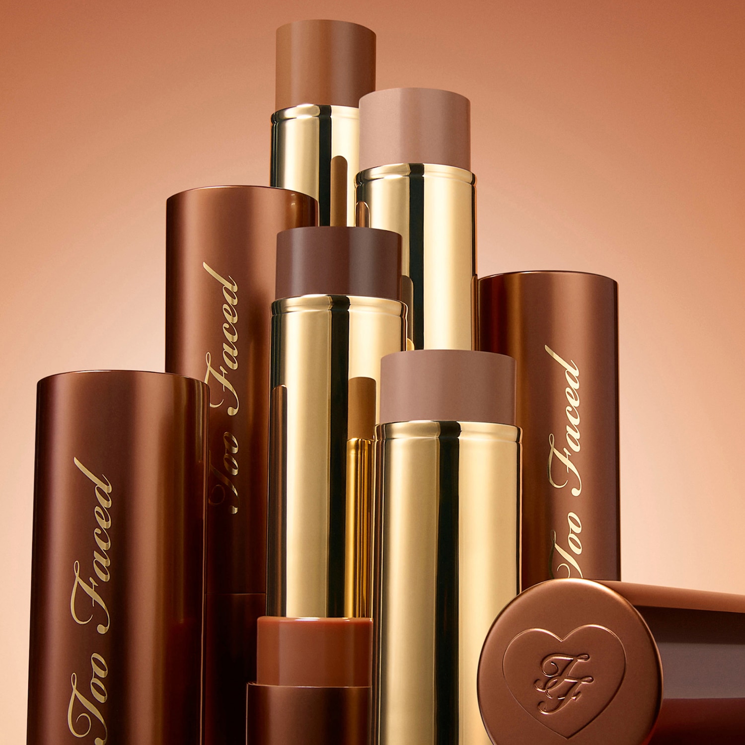 Eine Sammlung von Chocolate Soleil Melting Bronzing & Scultping Sticks von Too Faced in verschiedenen Brauntönen, die in einem gestaffelten Arrangement präsentiert werden.