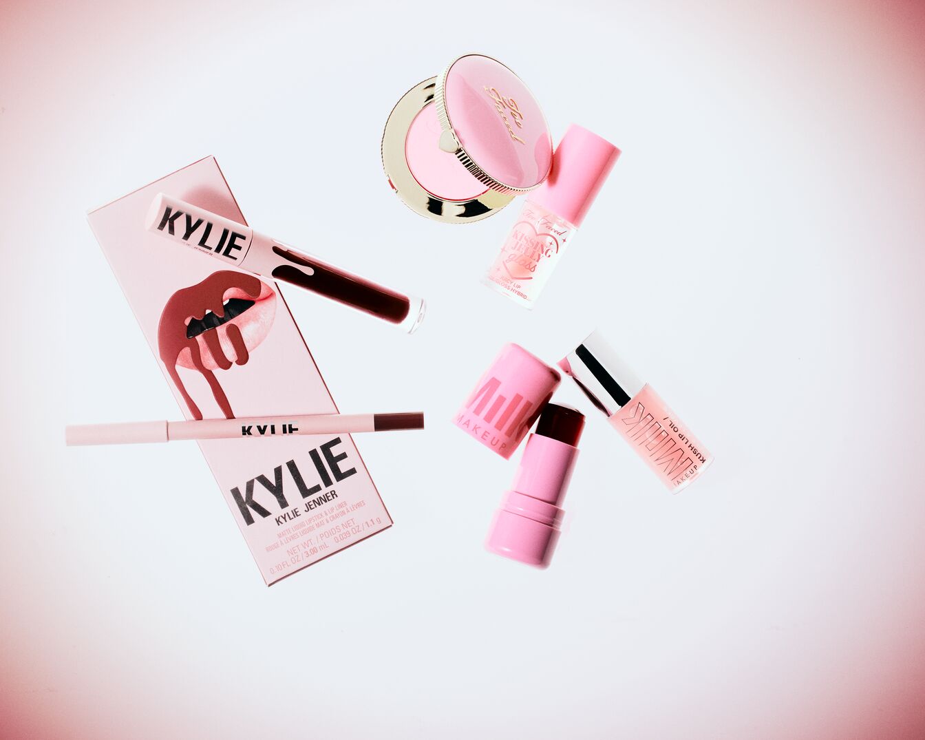 Eine Sammlung von Make-up-Produkten in verschiedenen Rosatönen, darunter Lippenstifte, Lipgloss und Rouge von Marken wie Kylie Jenner, Too Faced und Milk Makeup.