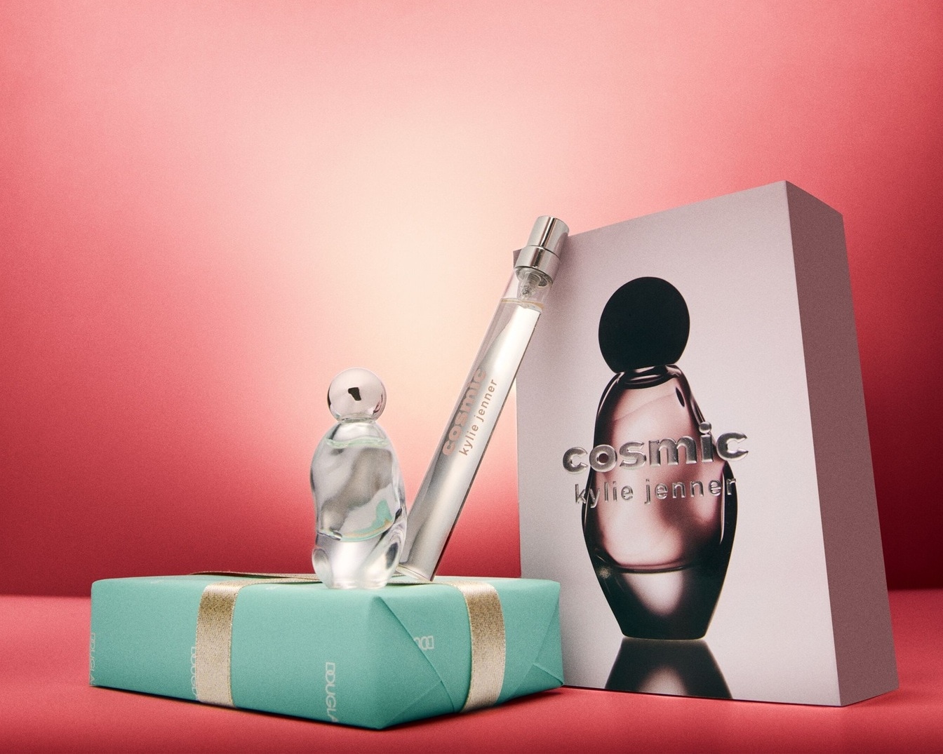 Kosmische Kylie Jenner Düfte präsentiert: Ein Geschenkset mit einem kleinen Flakon auf einer türkisfarbenen Schachtel und einem schlanken Zerstäuber, neben einer Schachtel mit dem Aufdruck 'Cosmic Kylie Jenner'.