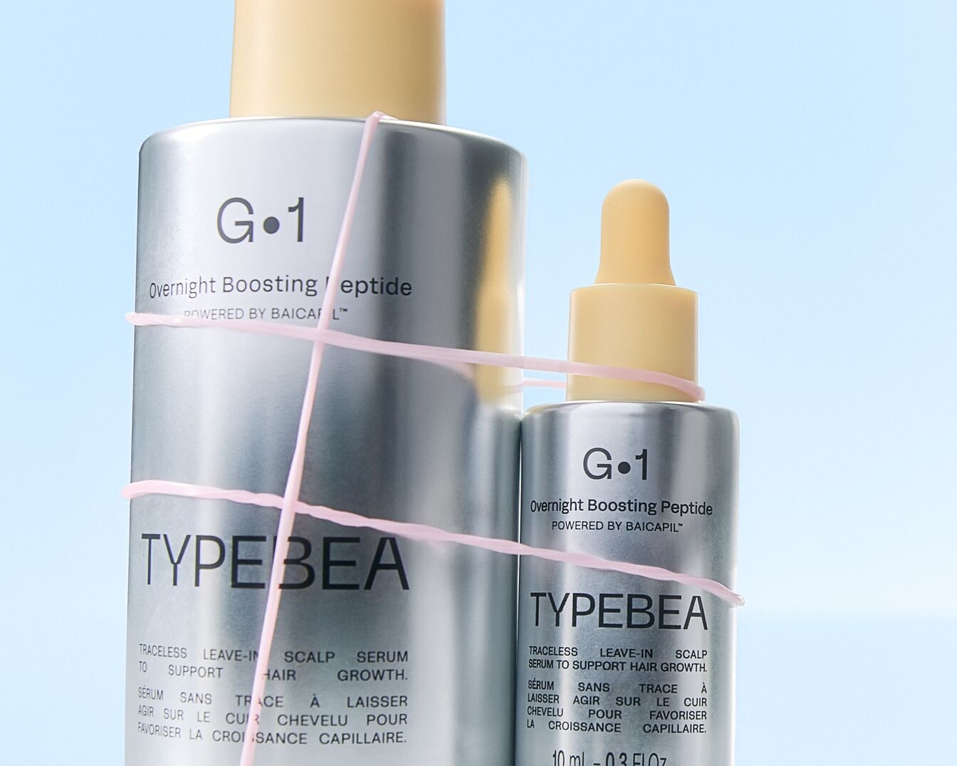 Twee zilveren flessen Typebea G-1 Overnight Boosting Peptide haarserum, omwikkeld met een roze touwtje, beloven een spoorloze leave-in behandeling voor de haargroei.