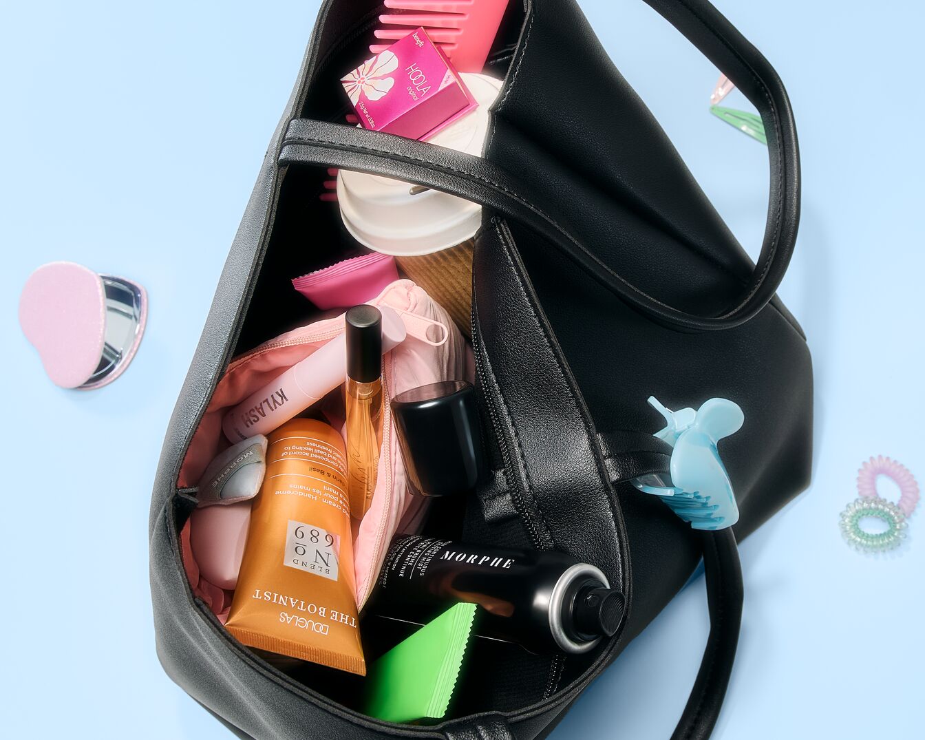 Een zwarte tas gevuld met diverse schoonheidsproducten zoals Hoola bronzer, Morphe setting spray, Douglas handcrème, Kylash en andere accessoires.