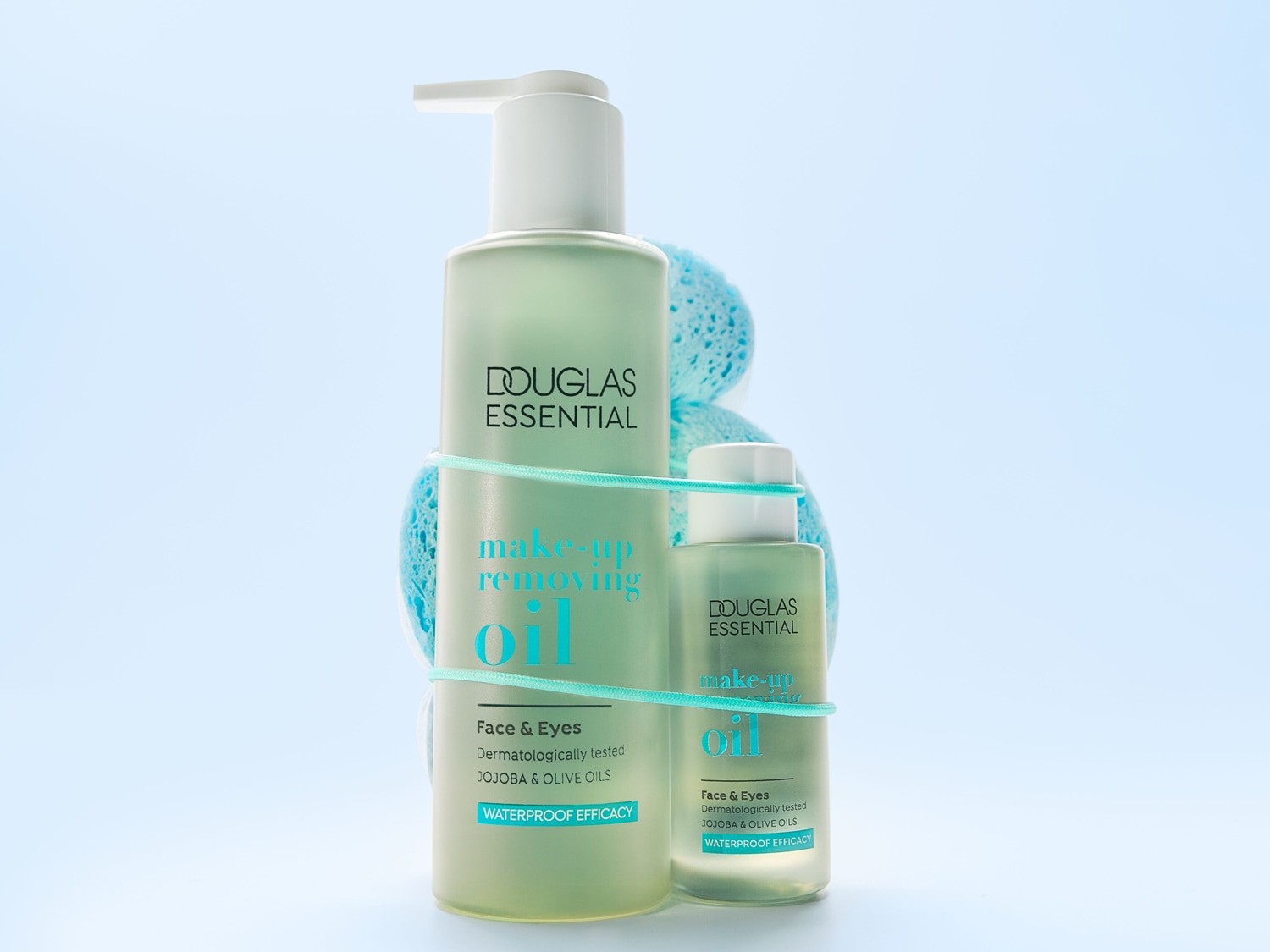 Twee flessen Douglas Essential make-upreinigingsolie, één groot met een pomp en één klein, zijn vastgebonden met een blauw elastiekje en een blauwe spons.