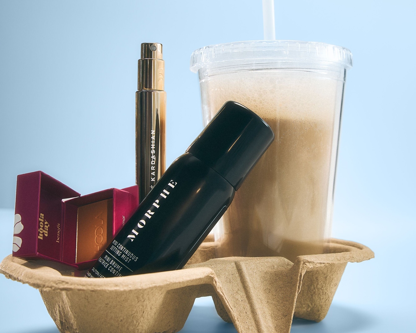 Een bruine kartonnen houder bevat Benefit Hoola Day bronzer, KKW Beauty parfum, Morphe Setting Mist en een ijskoffie.