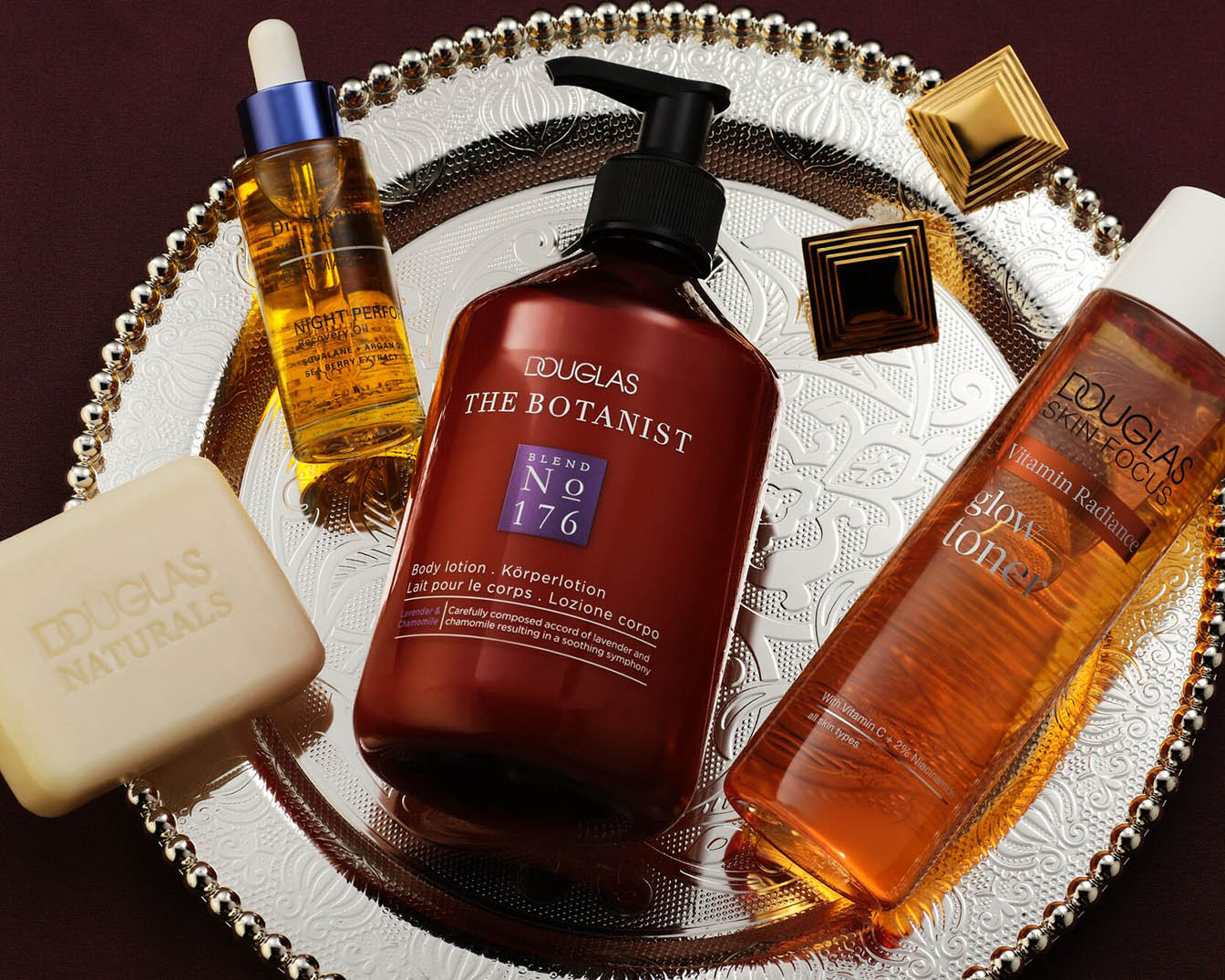Op een zilveren dienblad liggen Douglas Naturals zeep, The Botanist bodylotion, Skin Focus Glow Toner en Night Perf Recovery Oil, klaar om je huid te verwennen.