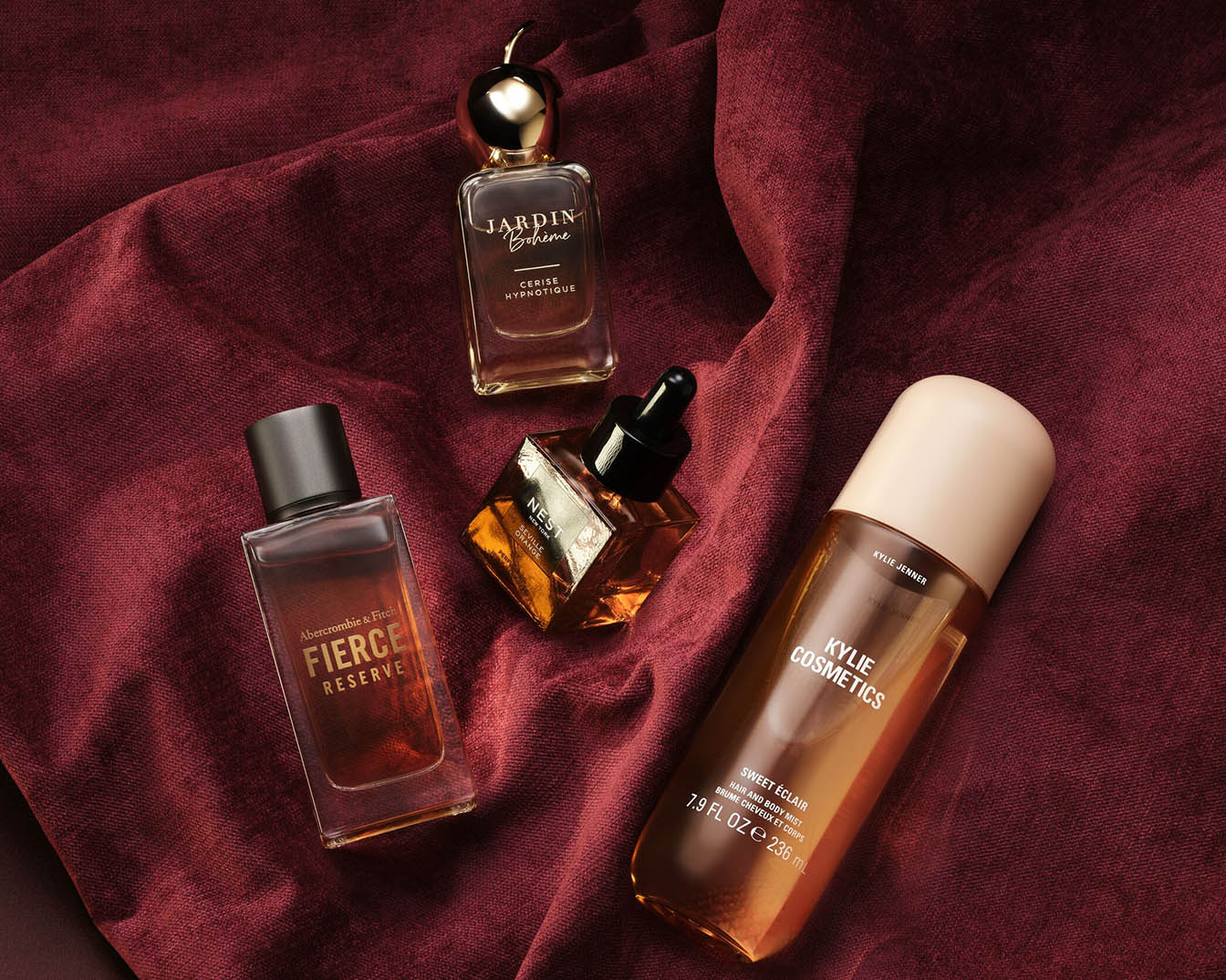 Auf einem burgunderroten Tuch liegen vier Parfümflaschen, darunter Jardin Bohème Cerise Hypnotique und Abercrombie & Fitch Fierce Reserve.