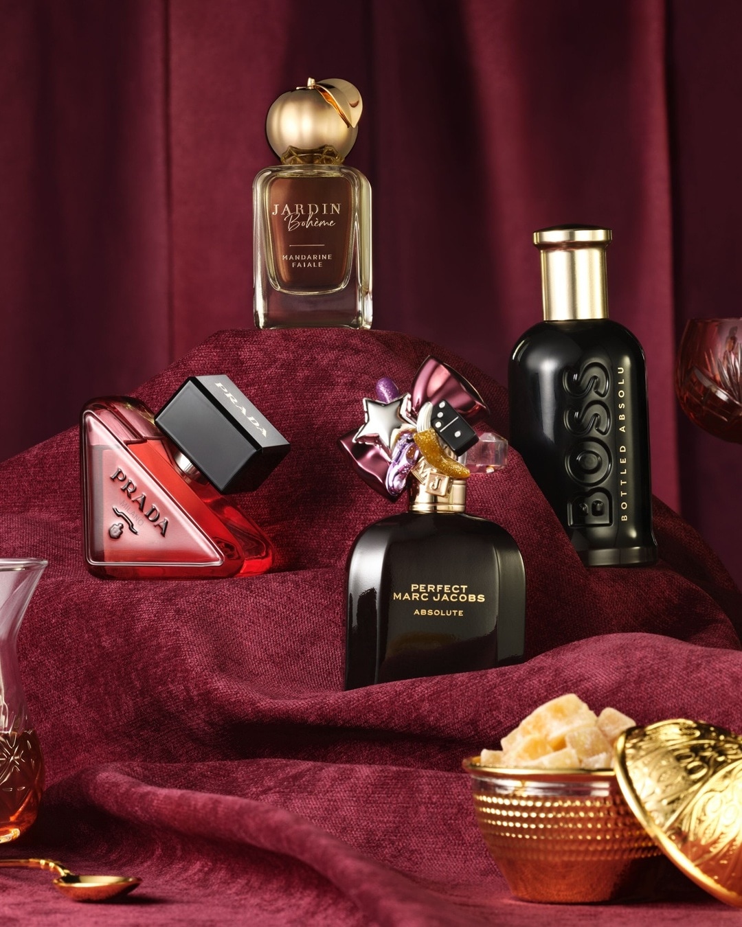 Eine Auswahl an Parfums, darunter Jardin Bohème, Prada, Perfect Marc Jacobs Absolute und Boss Bottled Absolu, präsentiert auf einem burgunderroten Stoff.