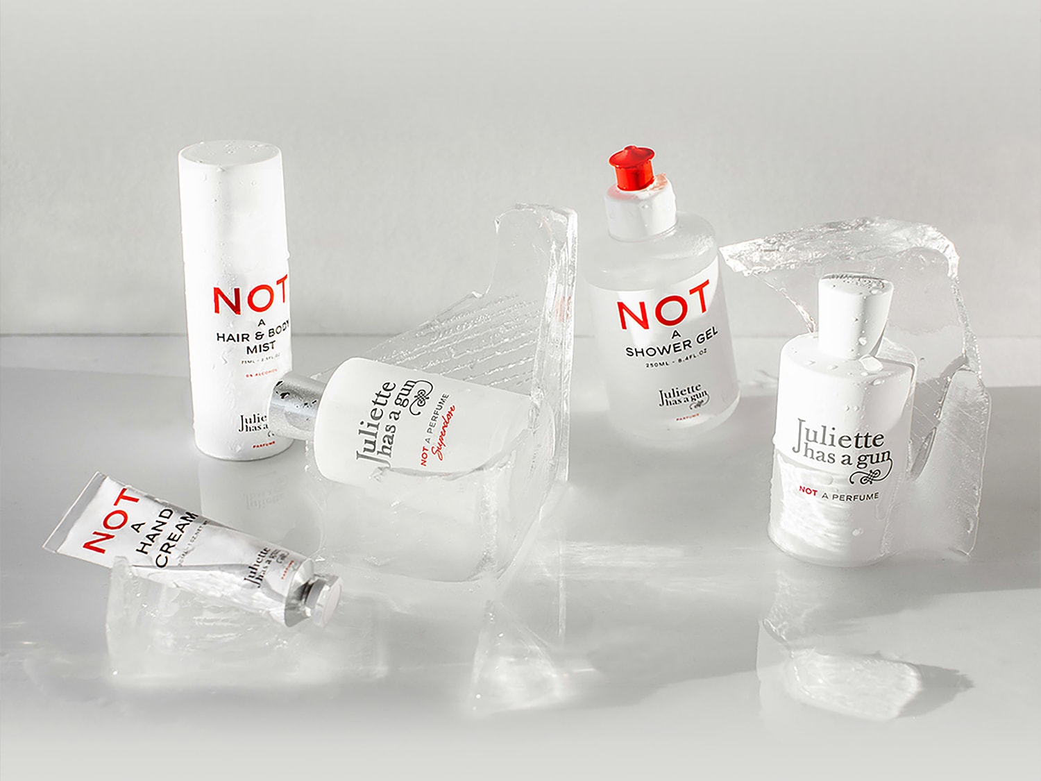 Eine Kollektion von Juliette Has a Gun-Produkten, darunter Handcreme, Haar- und Körperspray, Duschgel und Parfüm, alle in schlichten weißen Flaschen mit roten Akzenten, die für einen frischen und belebenden Duft sorgen.