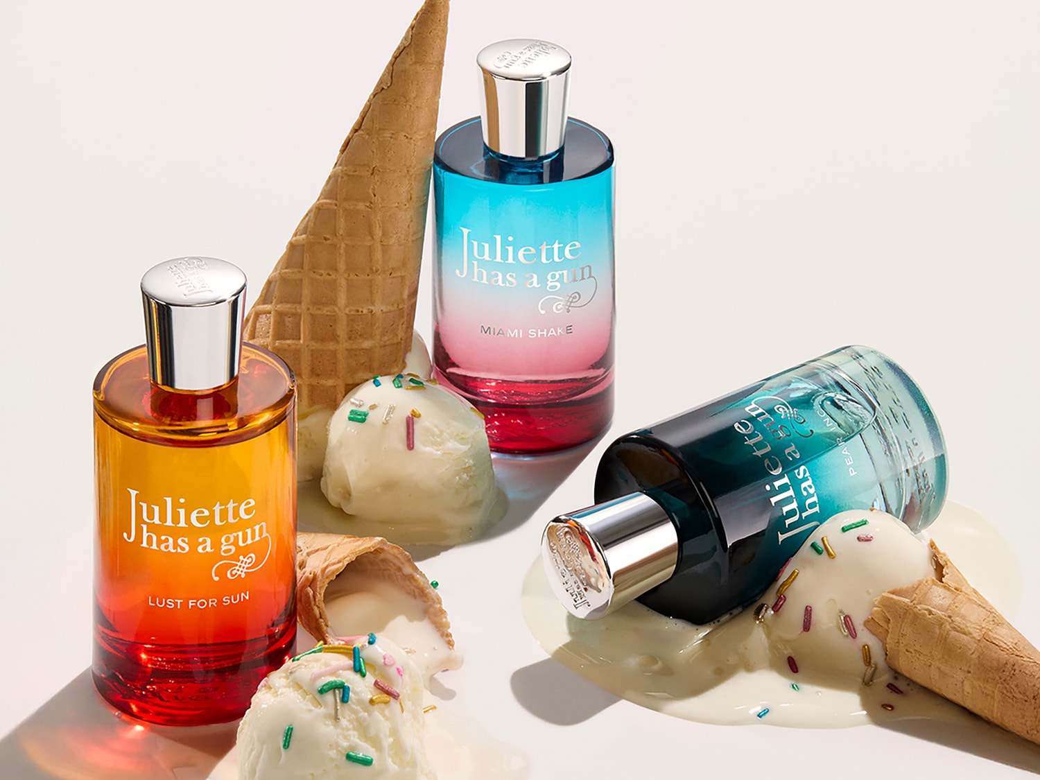 Drei Parfümflaschen von Juliette has a Gun, umgeben von Eistüten und Kugeln, die in den Sorten Lust for Sun, Miami Shake und Pear Inc. erhältlich sind.
