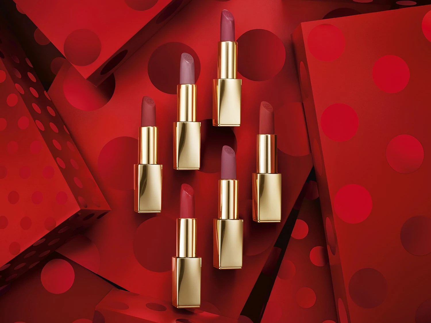 Découvrez une collection de rouges à lèvres aux teintes délicates, présentés dans des étuis dorés élégants, sur un fond rouge vif à pois, pour une touche de glamour.
