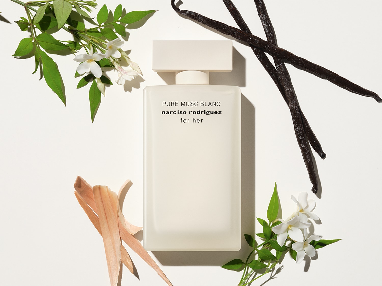 Ein rechteckiger, mattweißer Flakon "Pure Musc Blanc" von Narciso Rodriguez, umgeben von Jasminblüten, Vanilleschoten und hellem Holz.